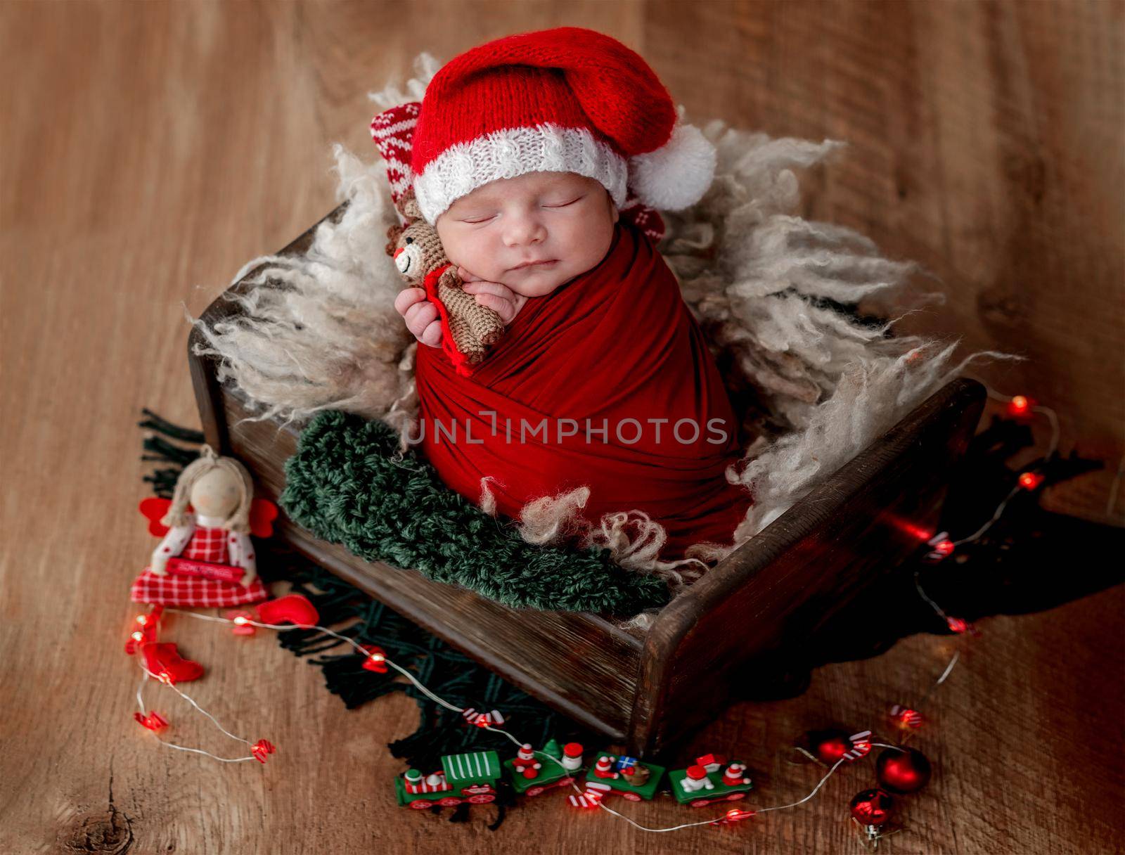 Cute newborn baby wearing santa hat and holding toy while sleeping in cradle with christmas decorations