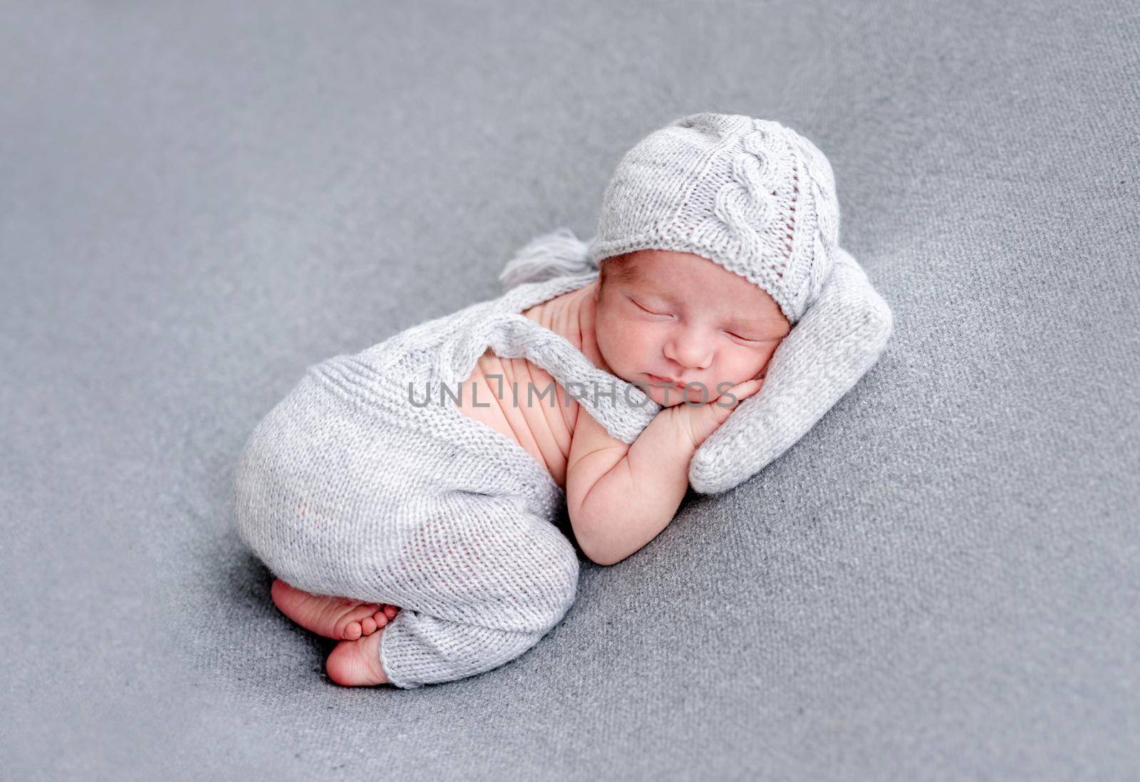 Charming newborn in knitted gray suit sleeping on tiny pillow