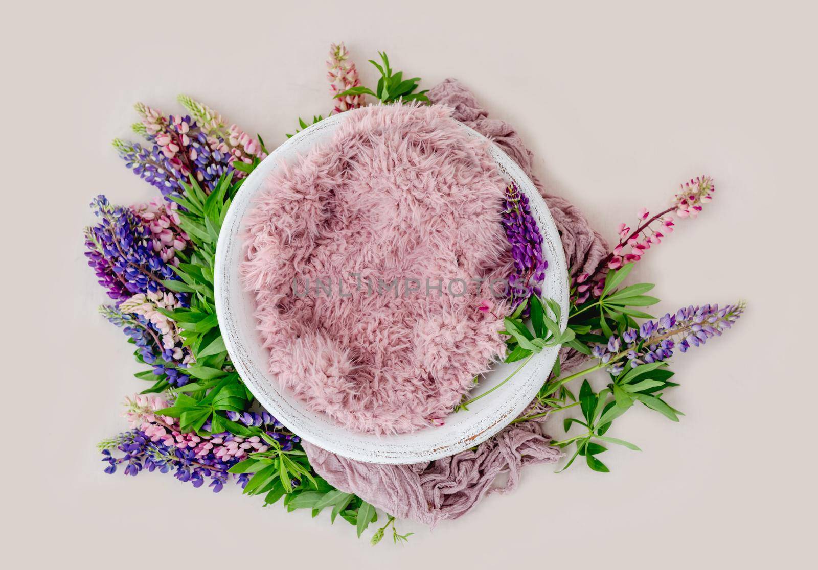Beautiful basin furniture for newborn studio photoshoot with pink fur and purple flowers decoration. Tiny designed place for infant photo