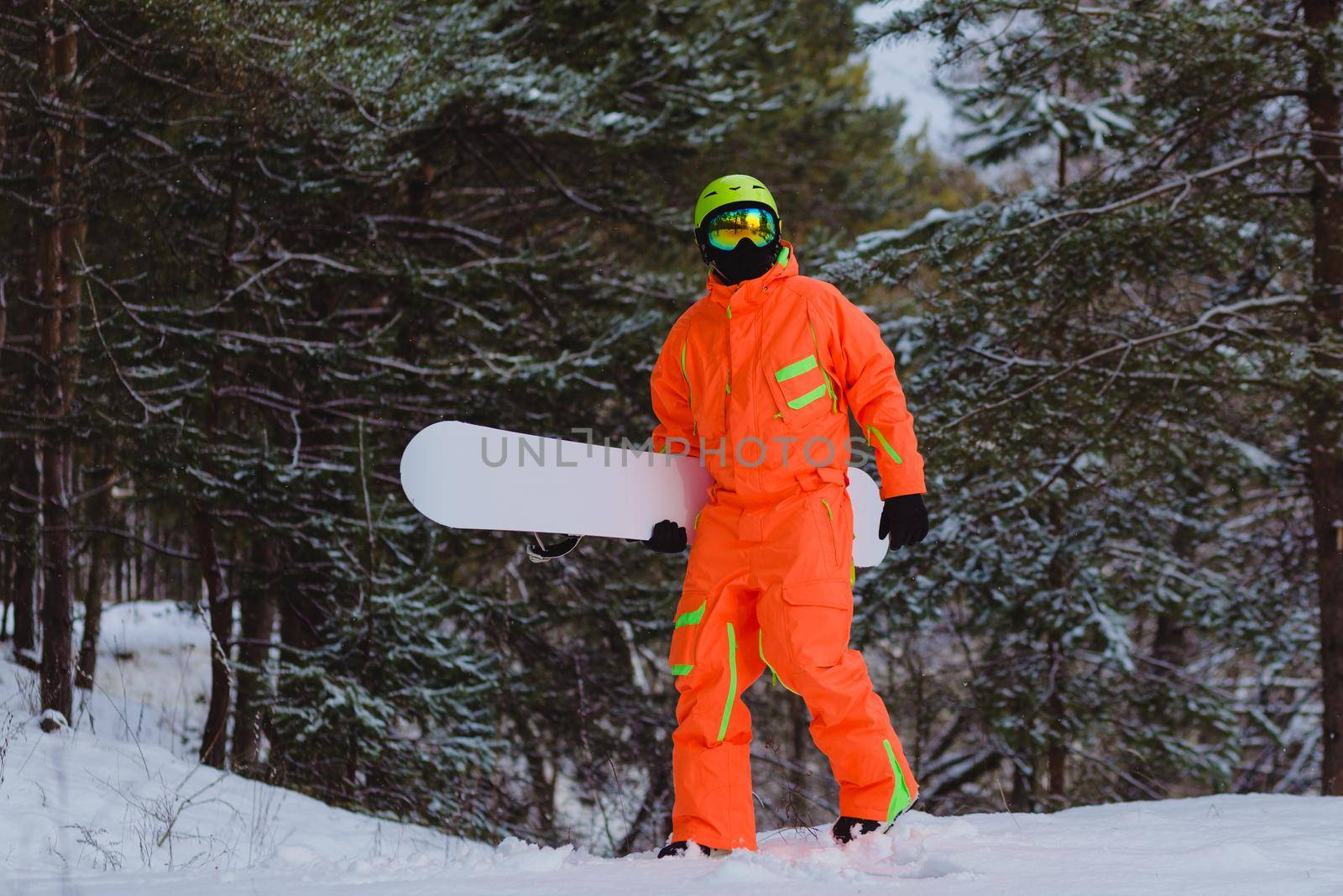 Snowboarder dressed in orange suit walking through the forest