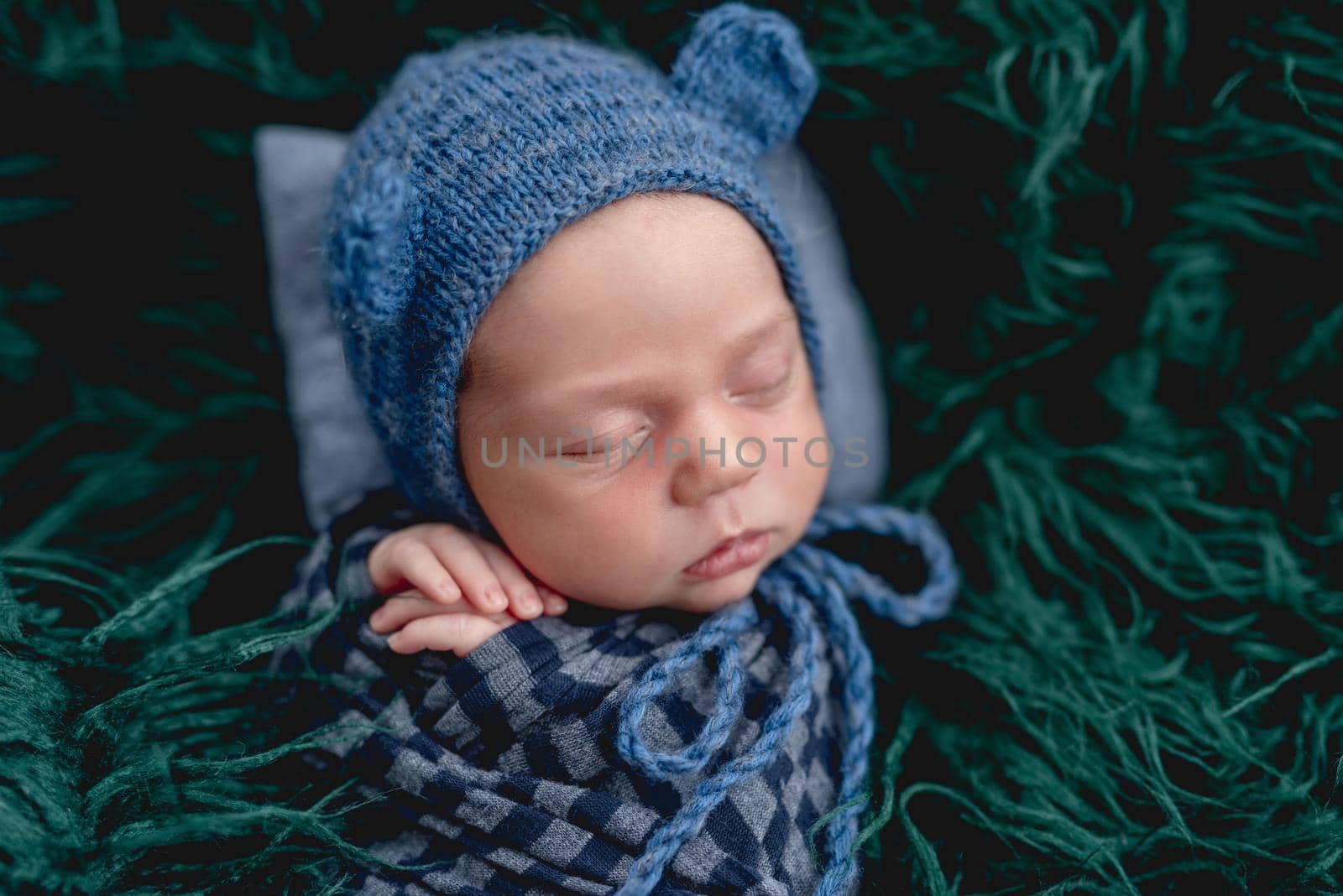 Cute sleeping newborn wearing blue knitted hat in the fur
