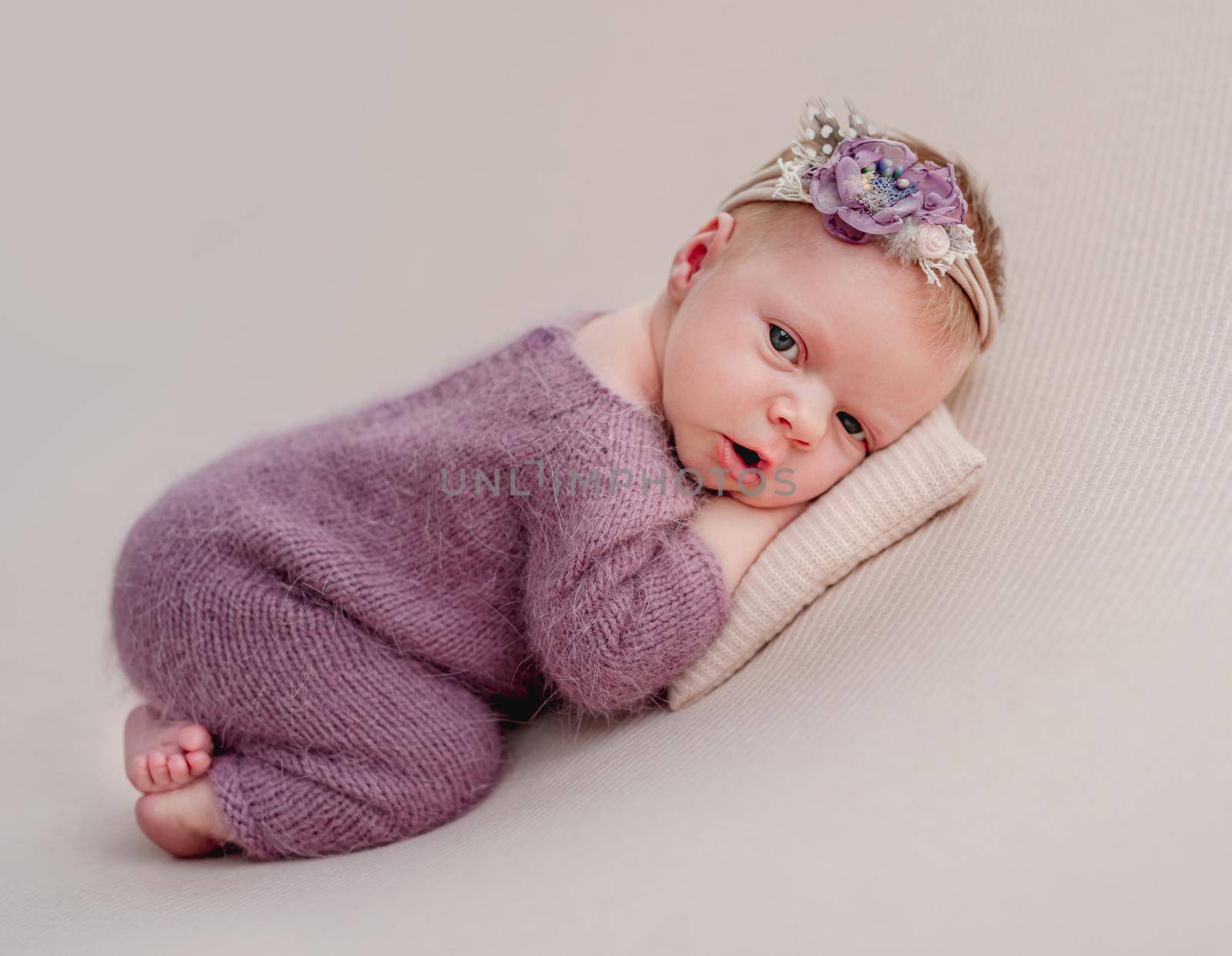 Awake newborn girl with flower diadem lying on tiny pillow