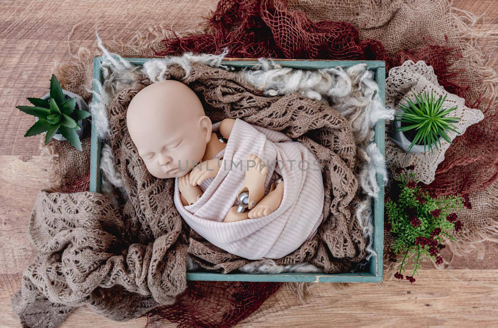 Beautiful background for newborn photosession with colorful plants and infant manequen for photographer trainings. Digital composite with wooden box filled with fur and standing on sackcloth