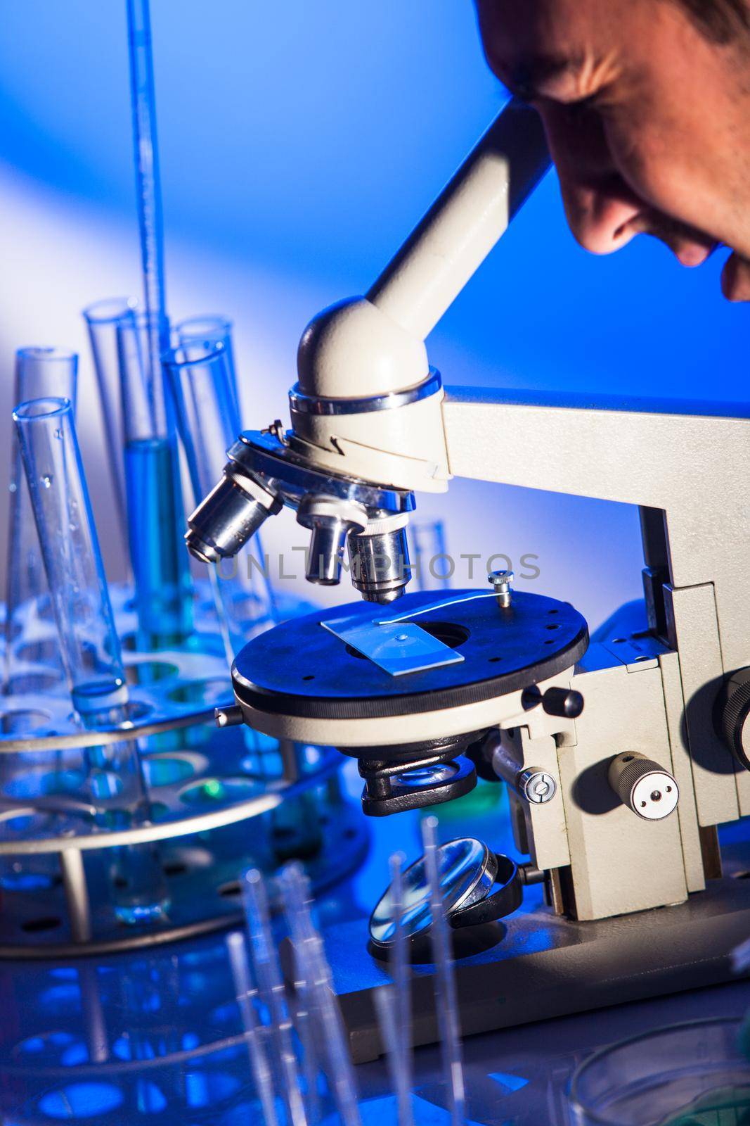 Man is looking into the ocular of microscope, doing reseach