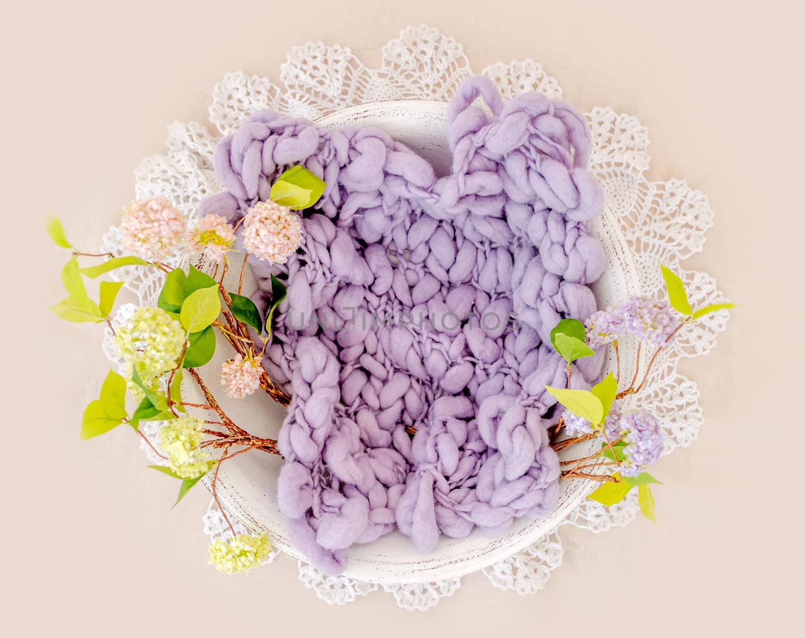 Beautiful backdrop for newborn photosession with flowers hydrangea. Digital composite with basin filled with knitted blanket isolated on light pink background. Top view