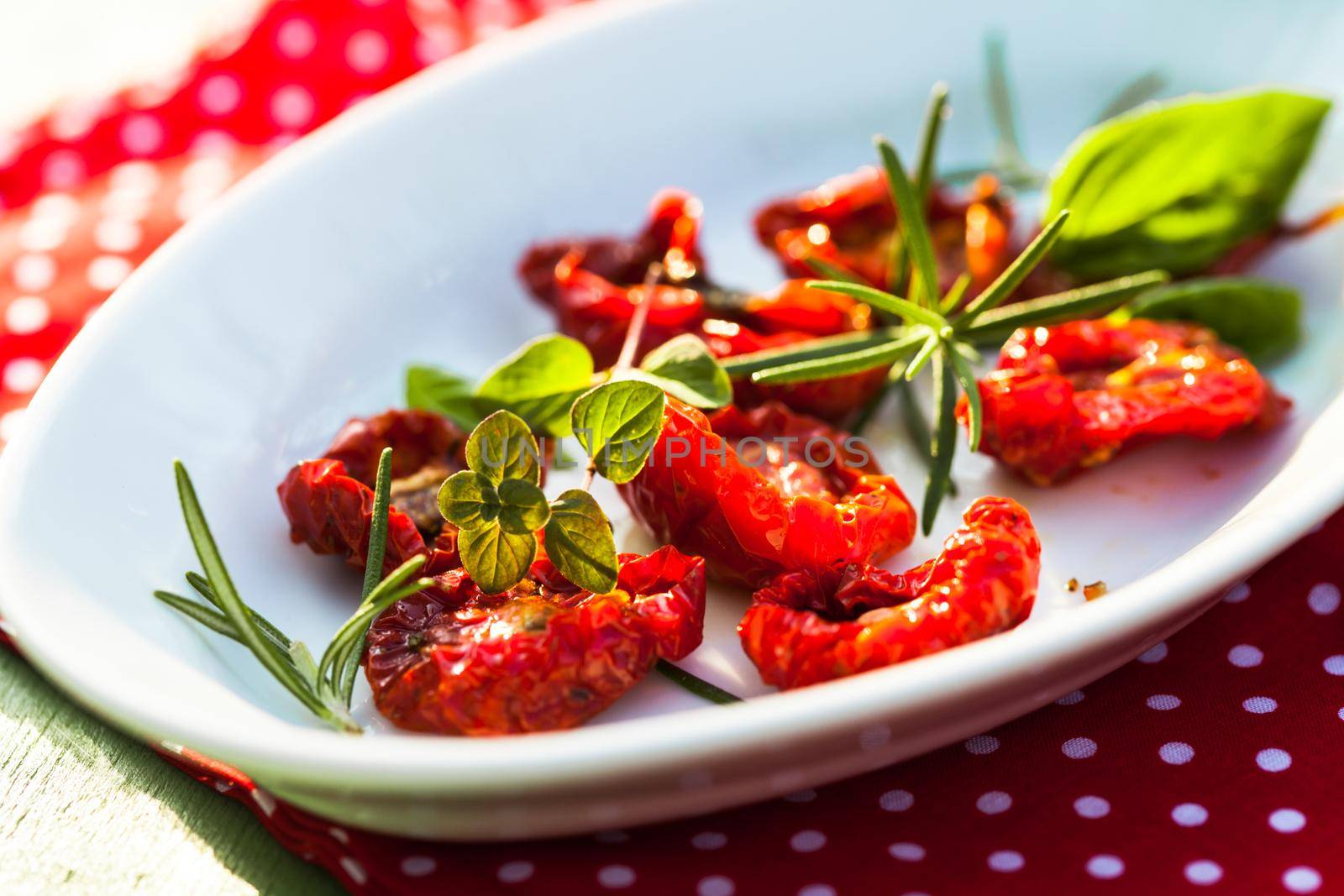 sun dried tomatoes on a white plate with fresh herbs - rosemary, basil and oregano