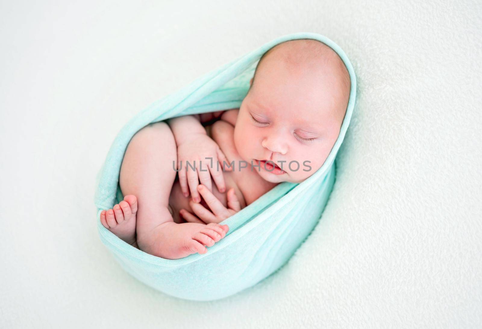 Adorable newborn baby girl lying on her back in the cocoon on white background and sleeping. Sweet infant child napping during studio photoshoot