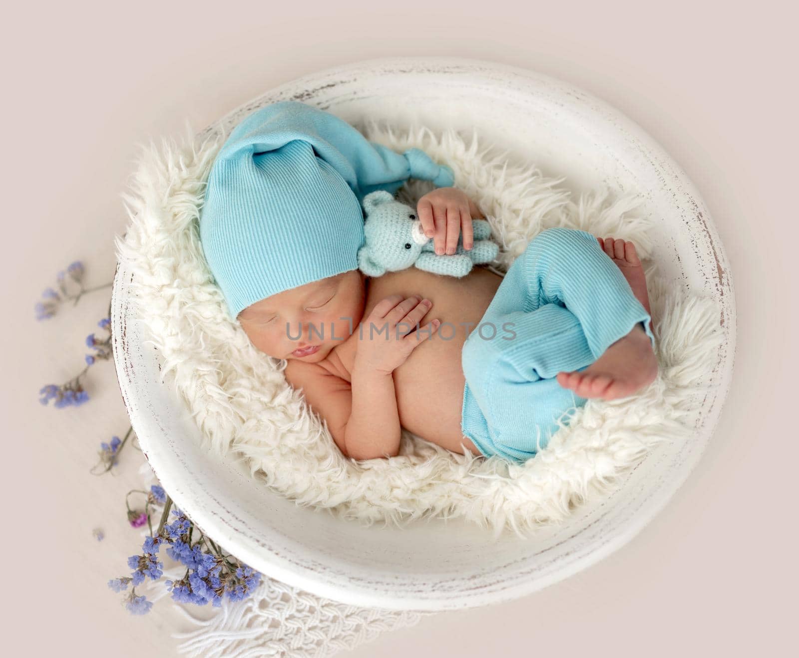 Sweet newborn with toy resting in white round cradle