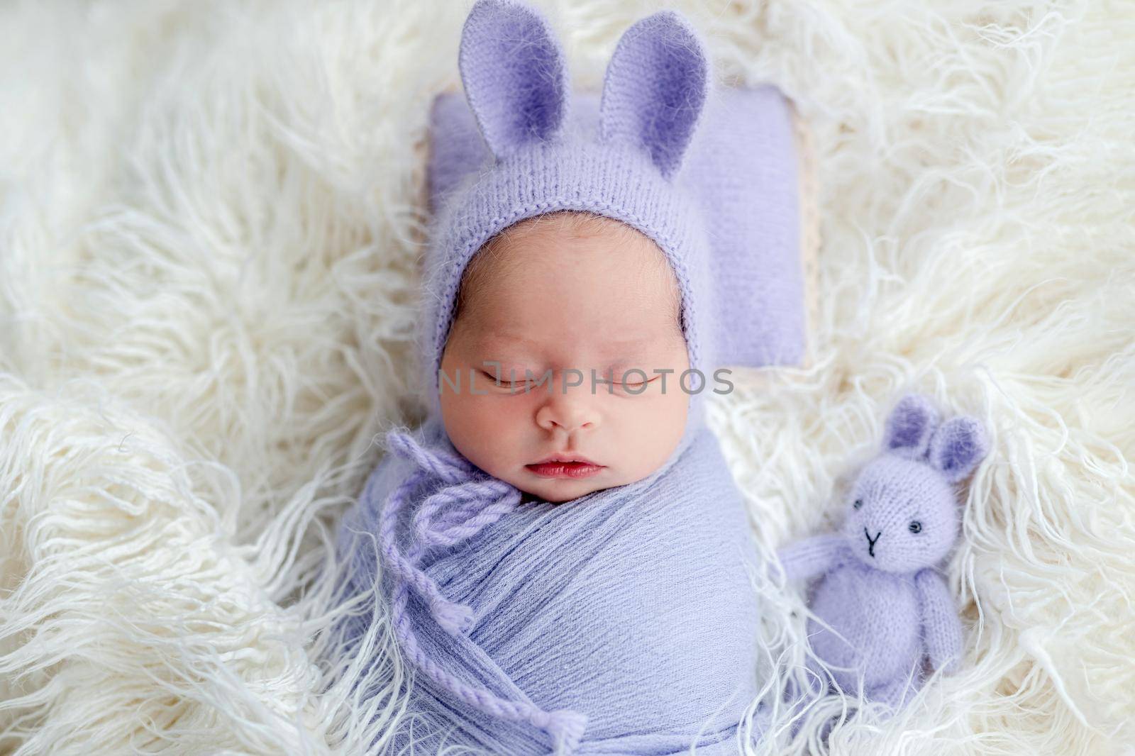 Cute newborn wearing hat with hare ears sleeping beside rabbit toy