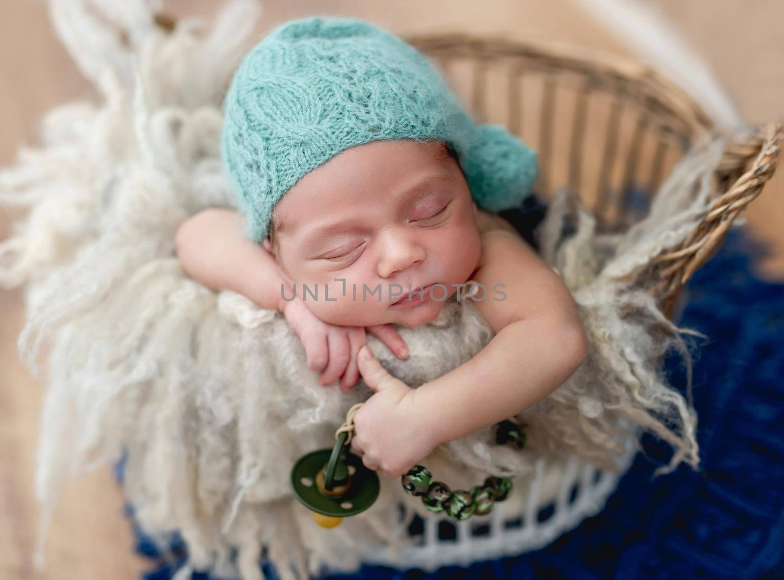 Charming newborn baby boy sleeping in basket with a pacifier in hand
