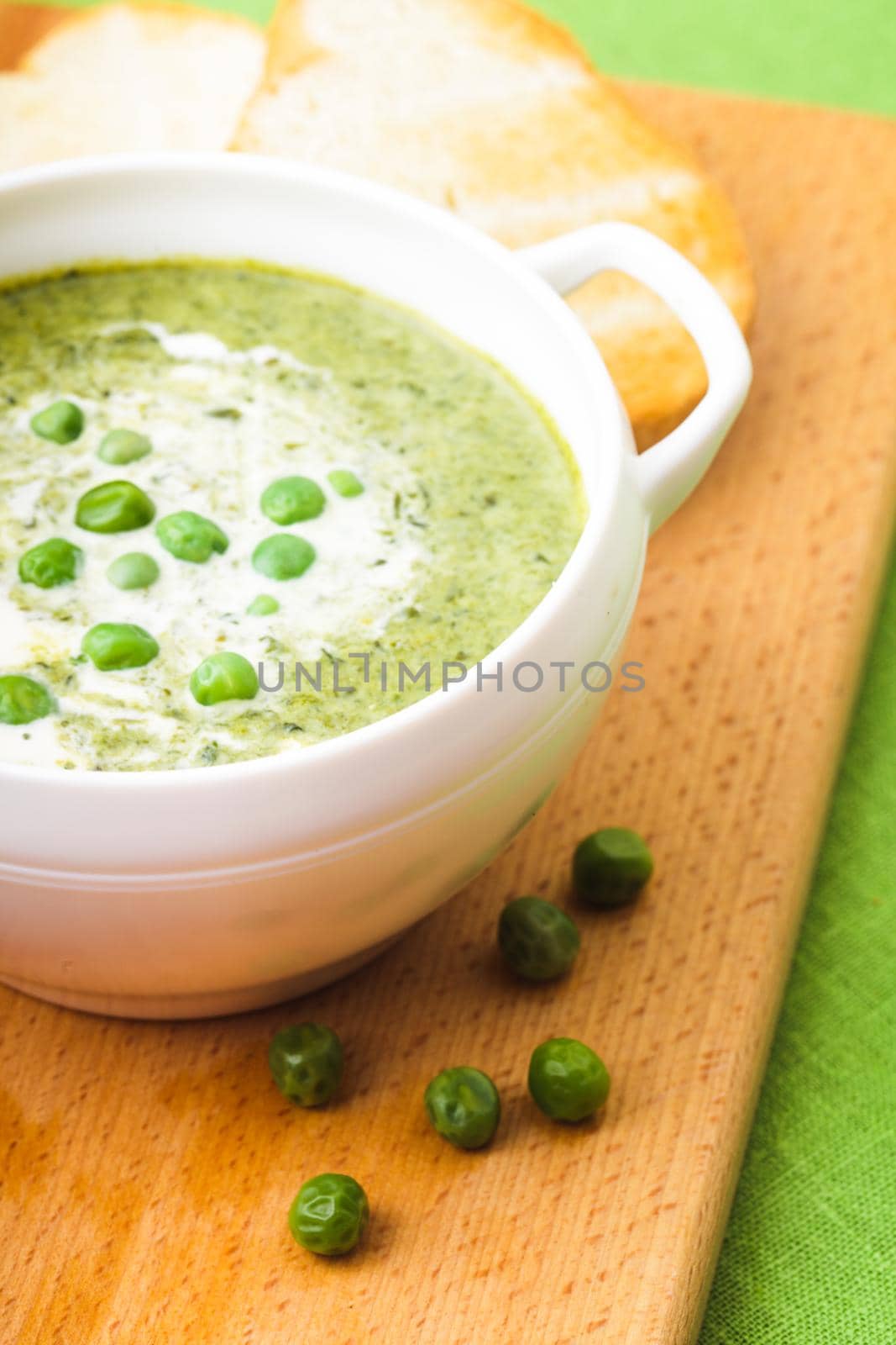 Fresh peas cream soup in a bowl on a wooden board and croutons