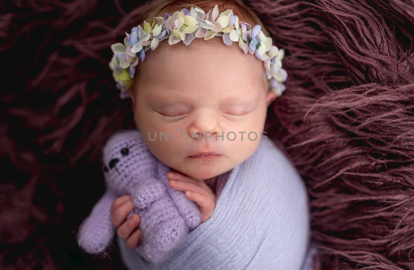 Newborn wearing floral diadem sleeping with knitted toy