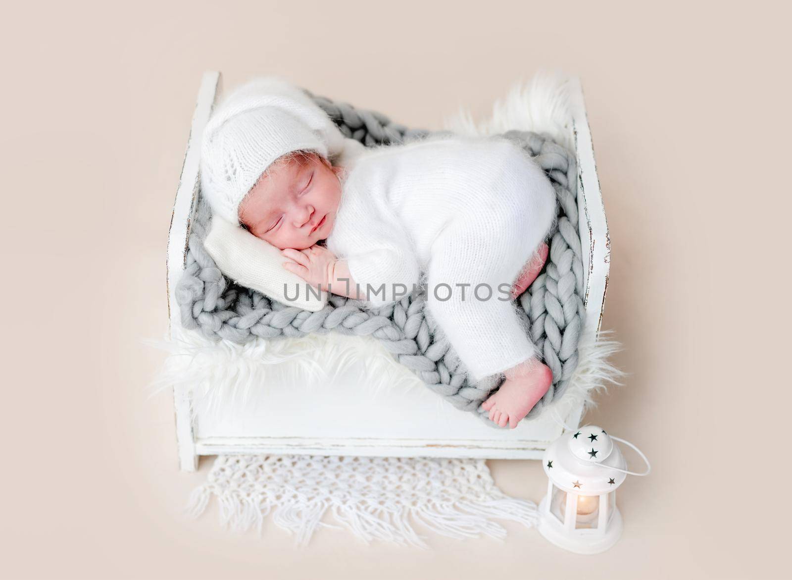 Cute newborn in white suit and hat sleeping on tiny bed