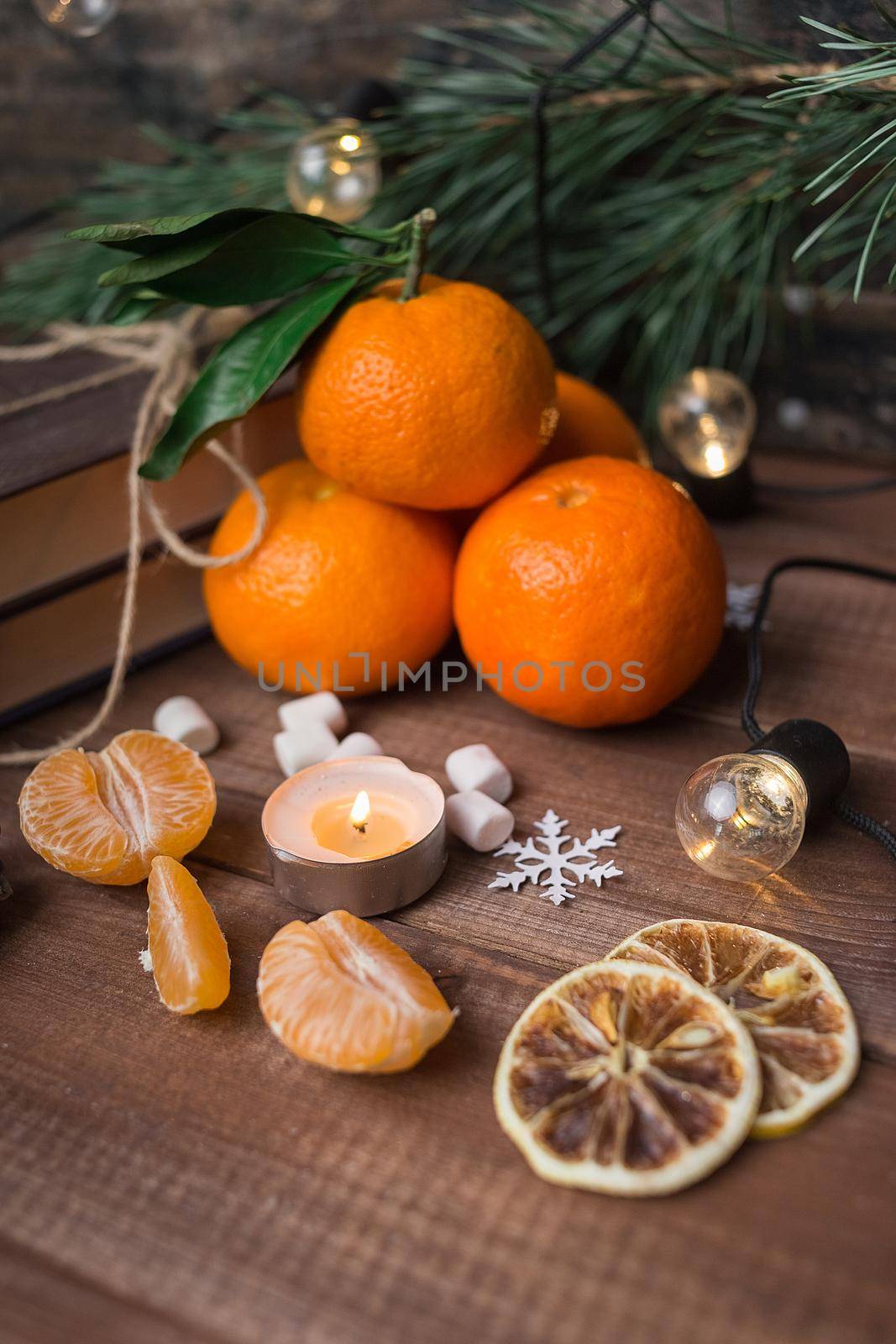 Christmas still life with fresh mandarines, marshmallows, lighted candle and garland on wooden background. Nature New Year concept in instagram style