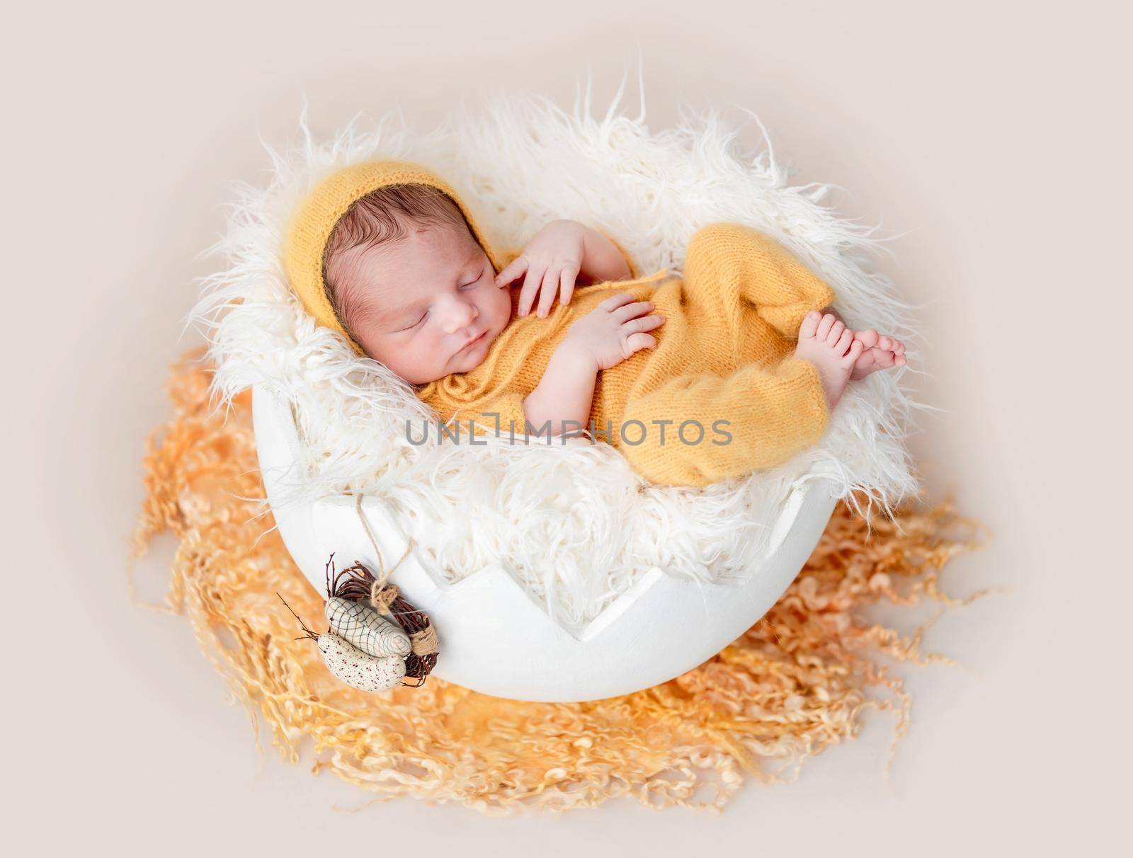 Cute newborn in yellow knitted suit lying in egg cradle