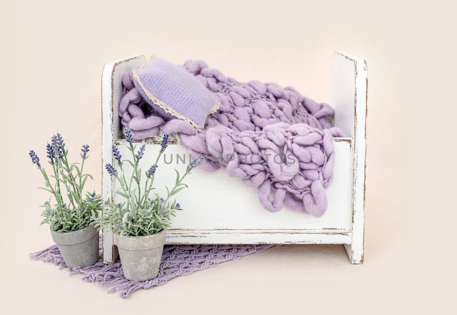 Beautiful white wooden bed furniture for newborn studio photoshoot with purple flowers decoration, pillow and knitted blanket. Tiny designed place for infant photo isolated on light pink background