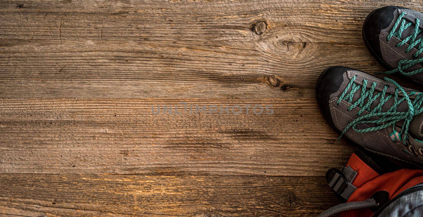 Trekking shoes, sunglasses and camera on wooden background with copy space, top view