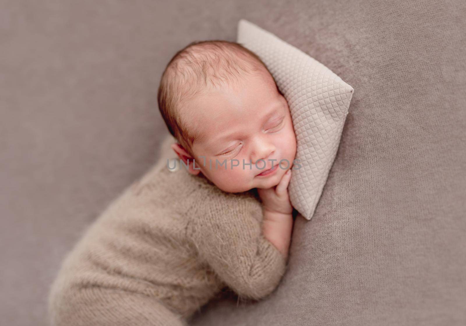 Cute newborn in knitted suit sleeping on tiny pillow