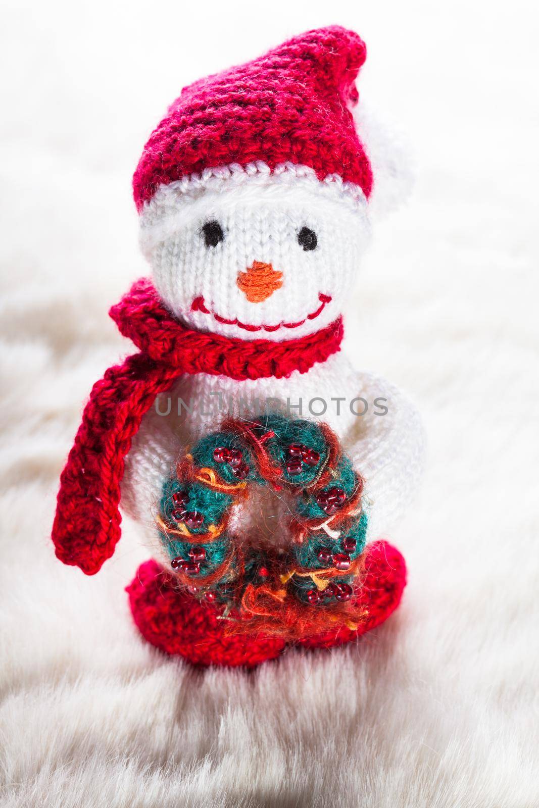 Knitted snowman with christmas wreath on white snow