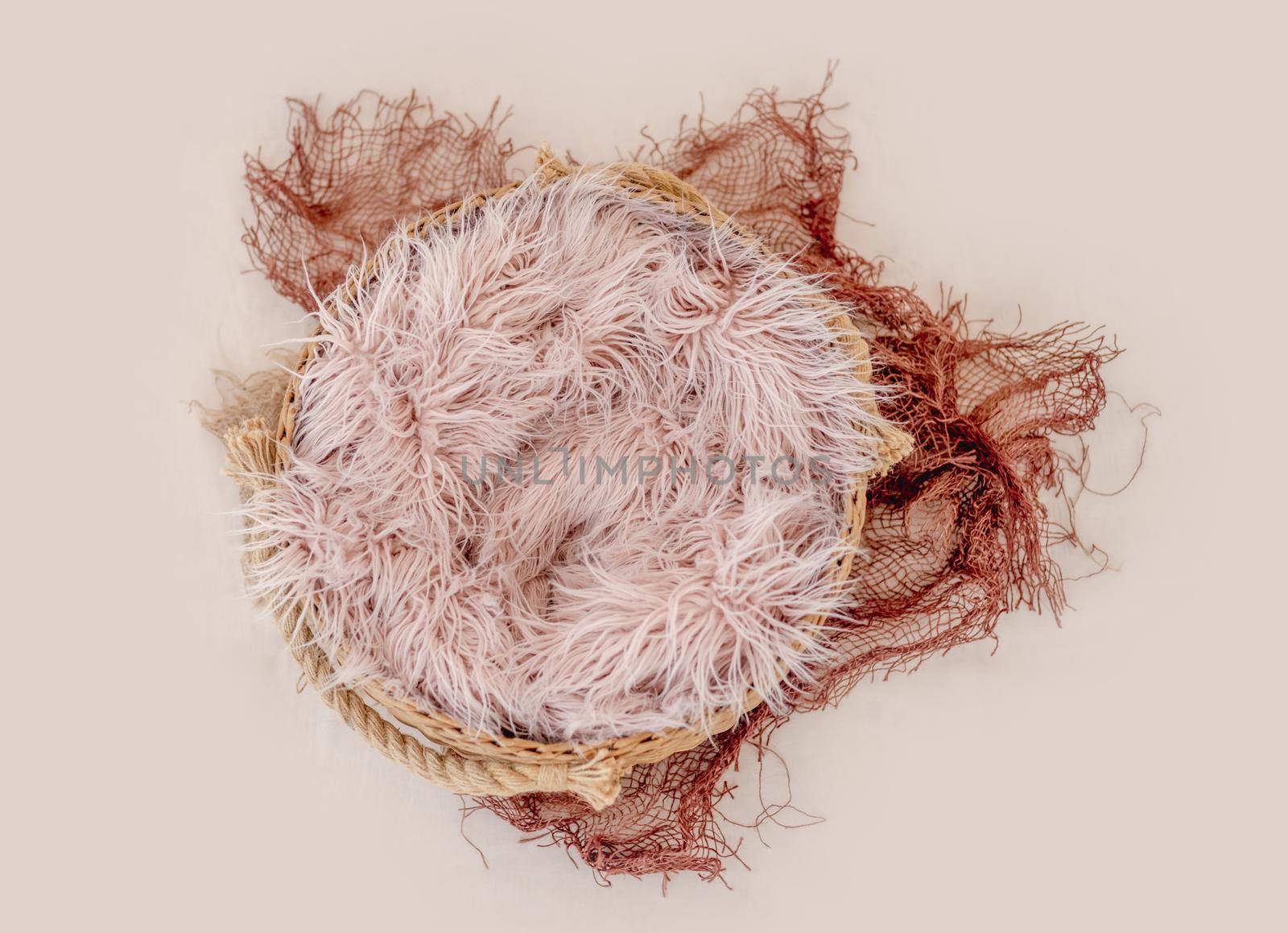 Beautiful backdrop for newborn photosession. Digital composite with basin filled with knitted blanket isolated on light pink background. Top view
