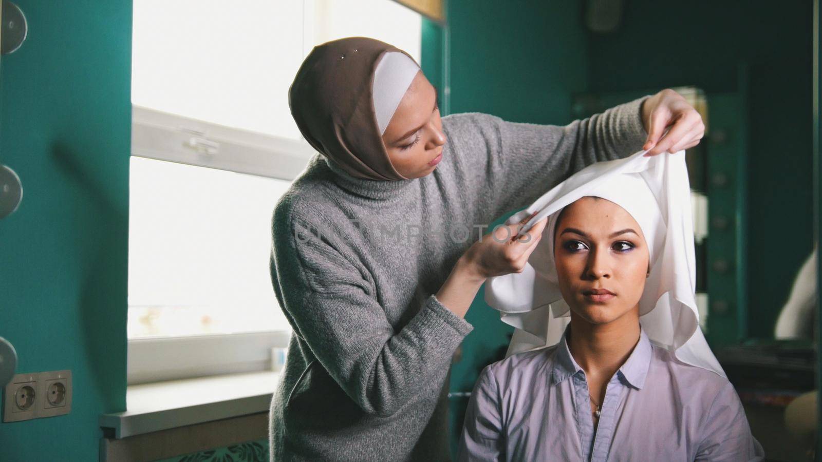 Two muslim women in front of a mirror to tie Islamic traditional turban, preparing for a wedding