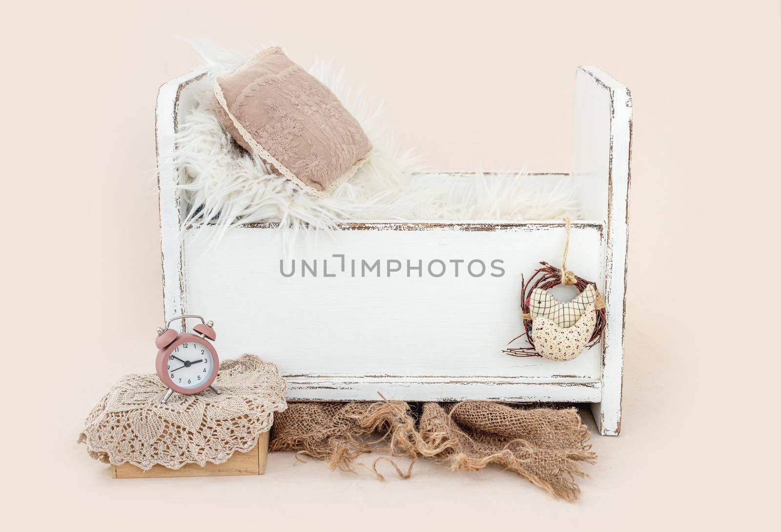 Beautiful white wooden bed furniture for newborn studio photoshoot with fur, pillow and clock decoration. Tiny designed place for infant photo isolated on light pink background