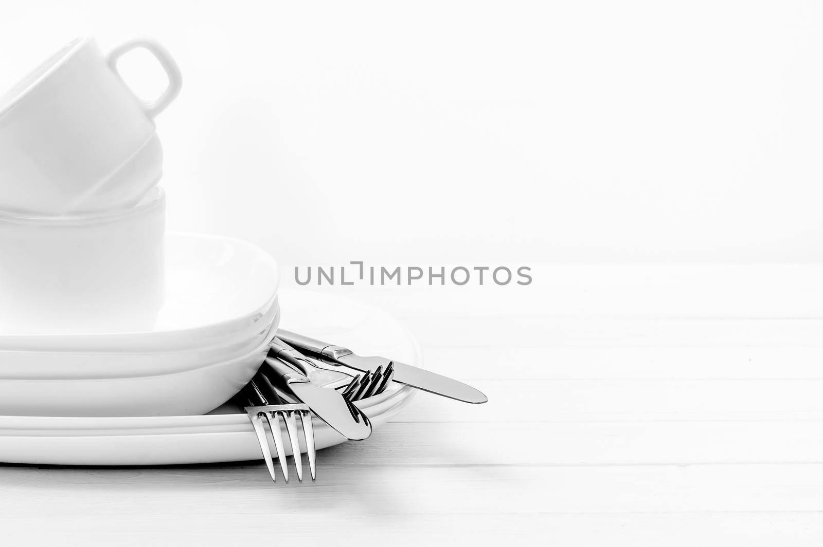 Empty white plates, cups and silver cutlery on light white background. Close-up