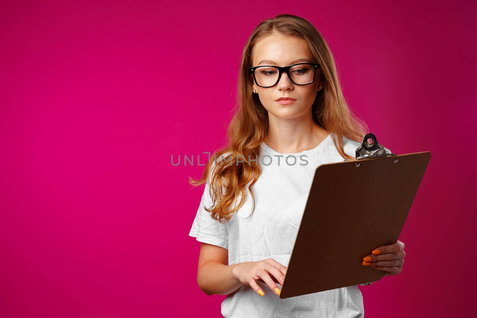 Young beautiful smiling woman standing and holding clipboard against pink background