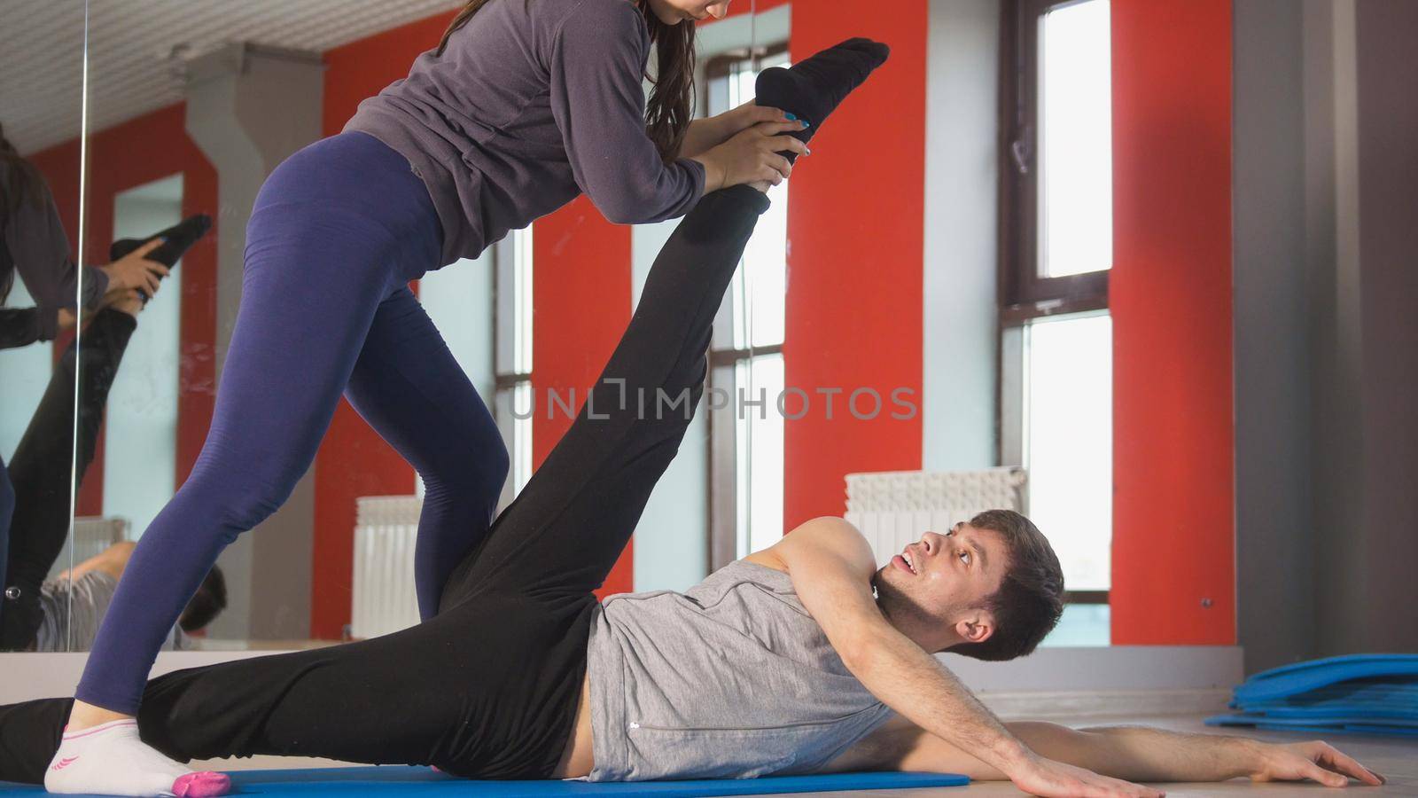 Female personal trainer help man with stretching exercise in front of mirror, close up