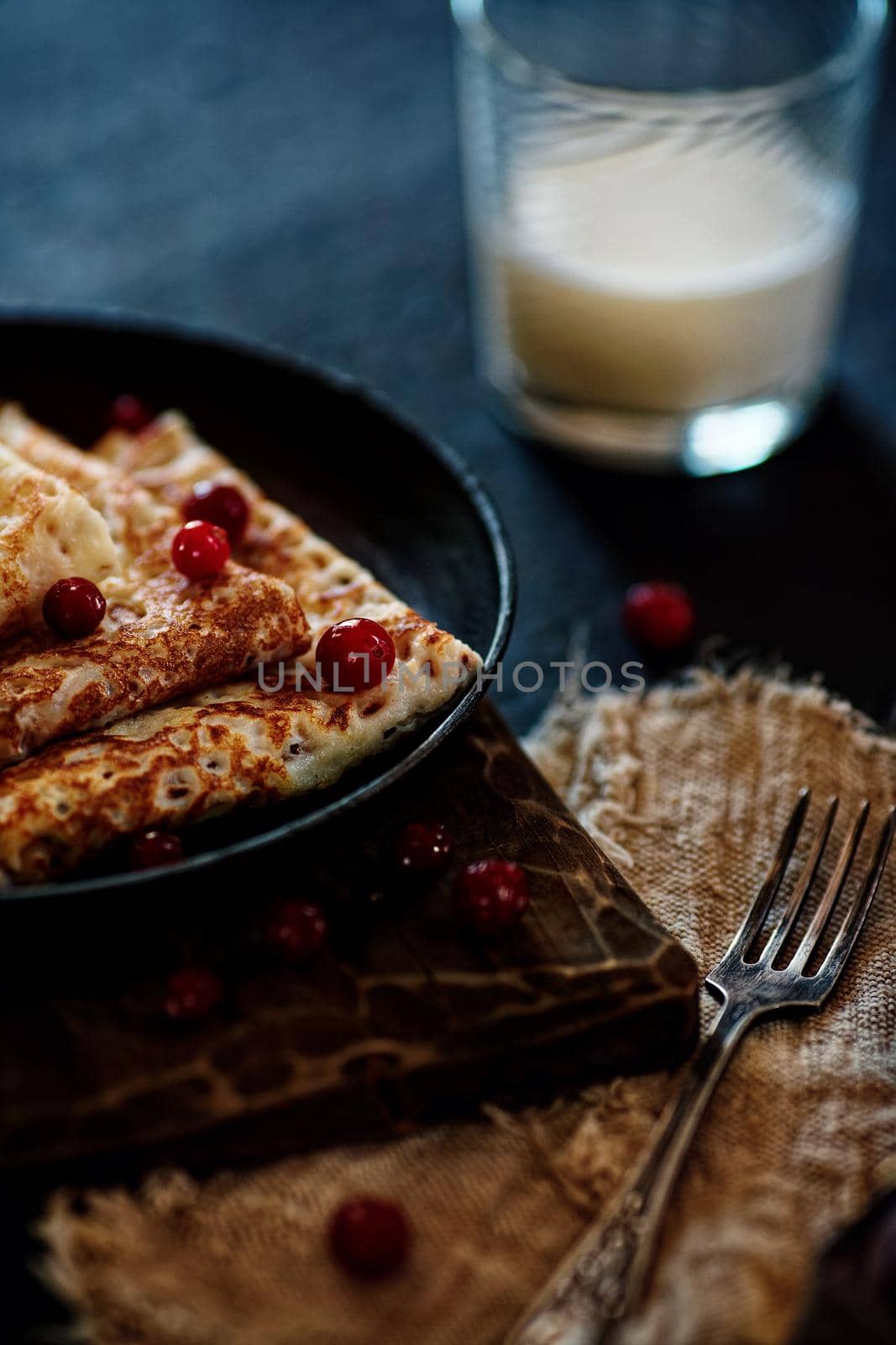 Delicious home-cooked food. Pancakes in a frying pan with cranberry berries and milk. National Russian cuisine. Rustic style by SergeyPakulin