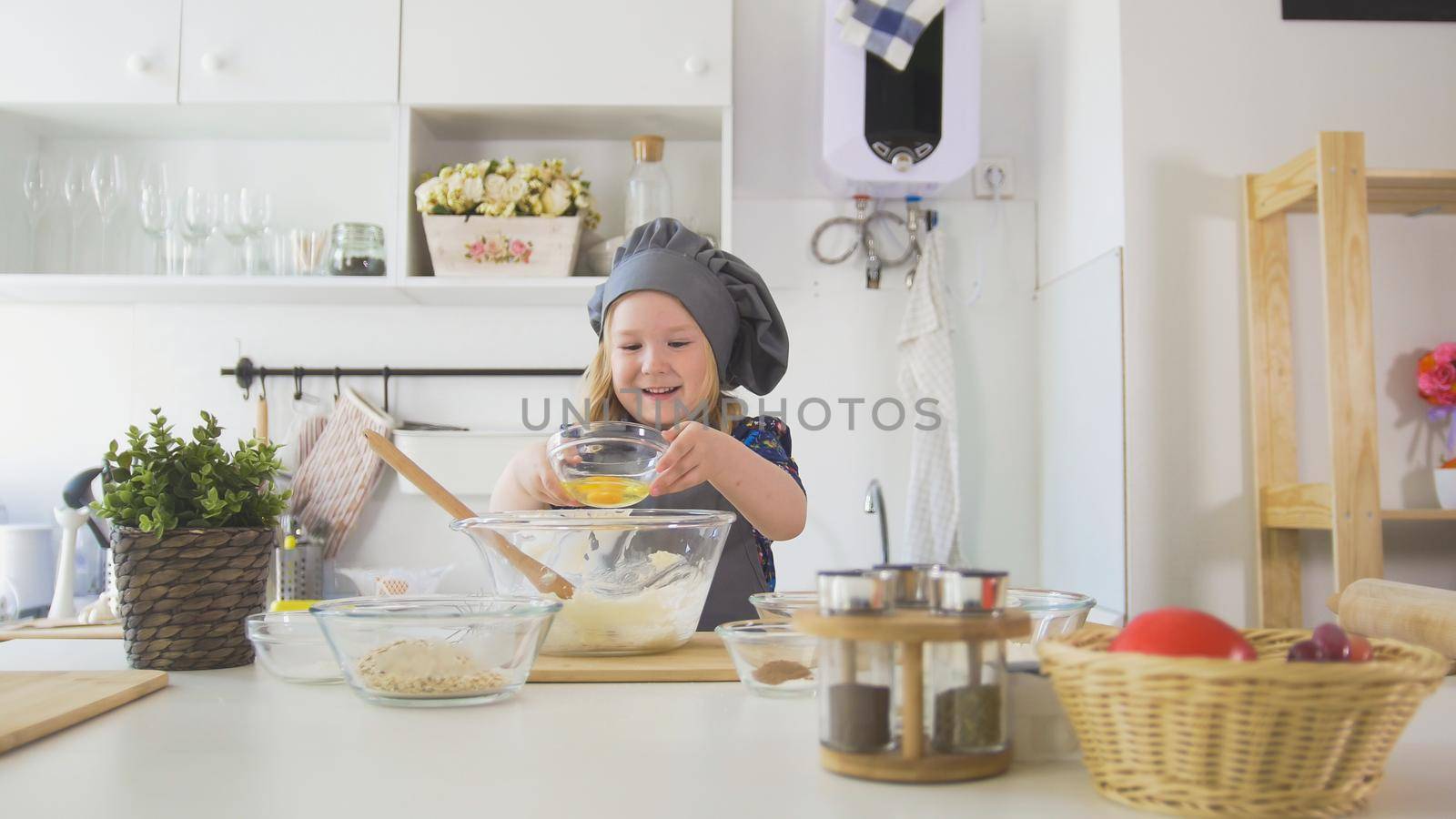 Little girl baker puts eags to the pastry dough for cooking biscuits, close up