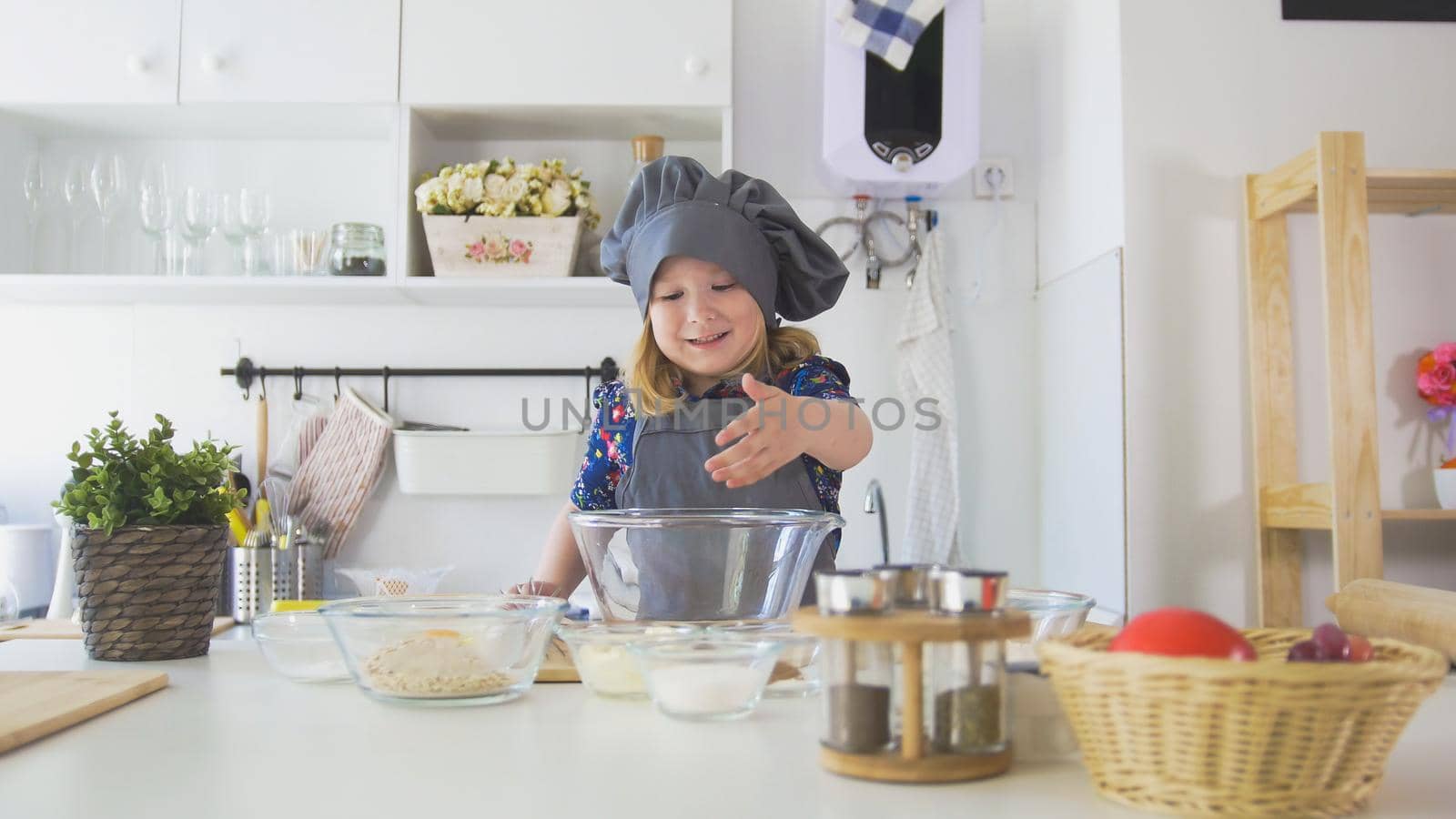 Cheerful little girl in apron rolls out the dough in the kitchen, close up