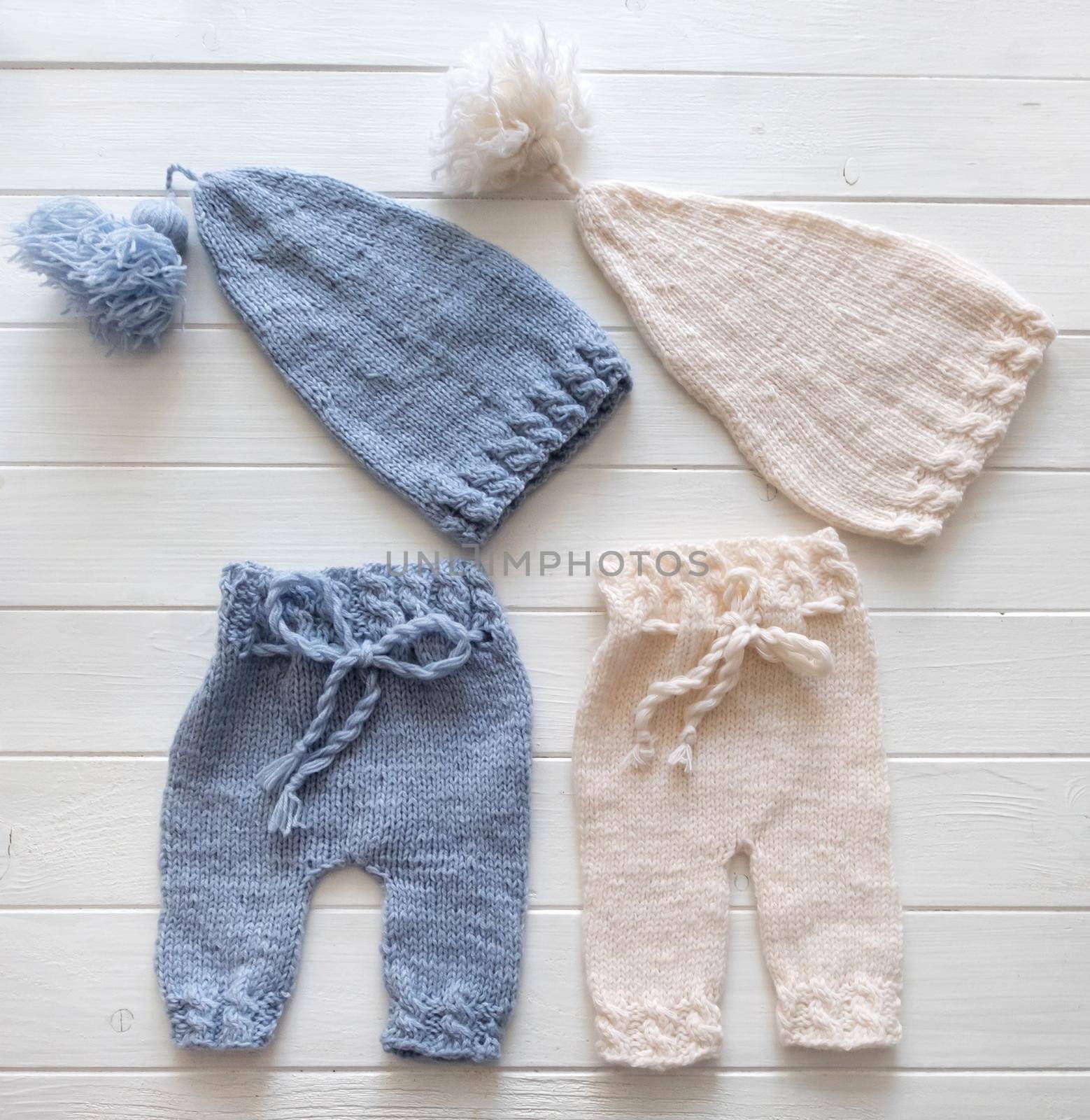 Cute blue and white knitted hats and pants for babies on the white table