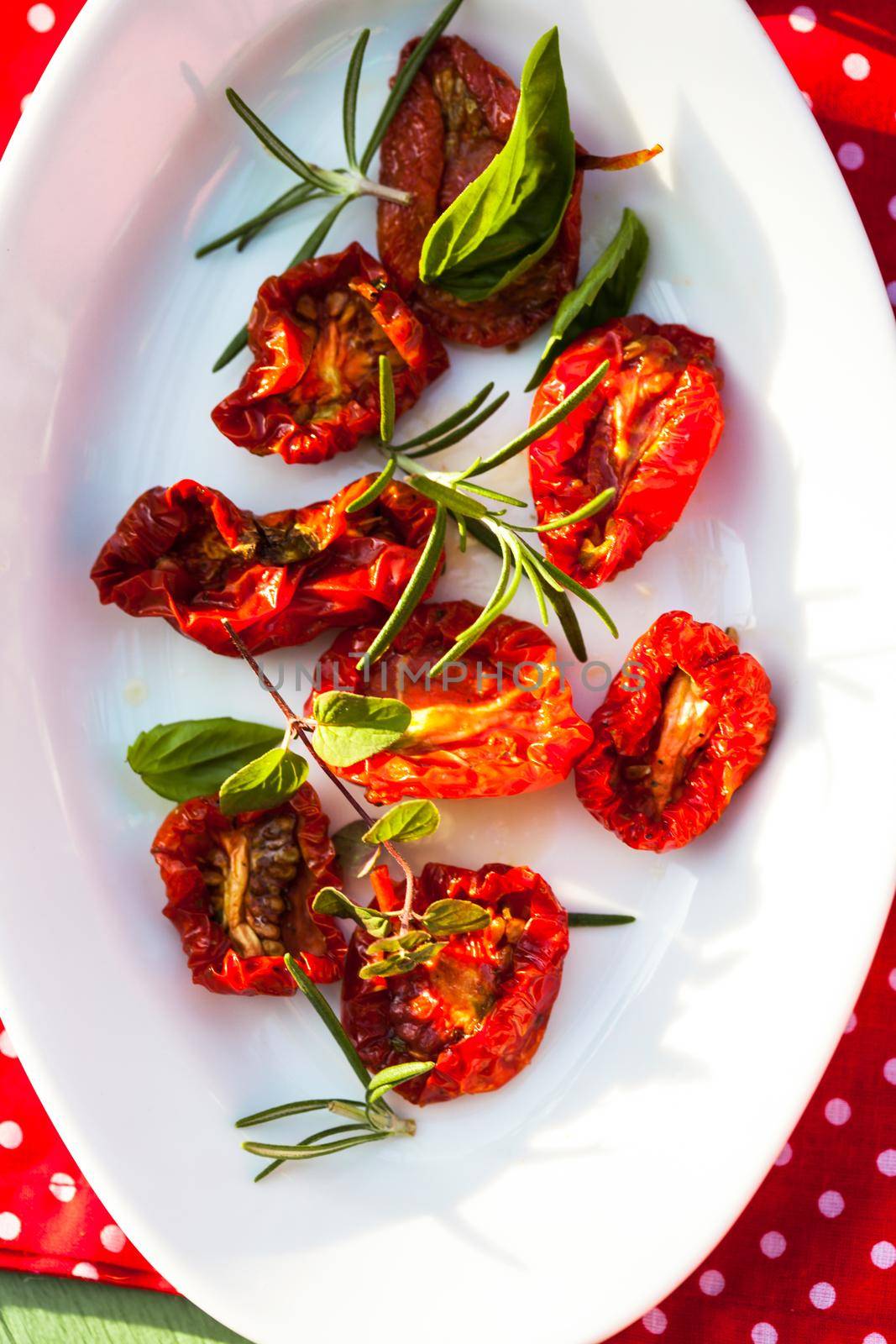 sun dried tomatoes on a white plate with fresh herbs - rosemary, basil and oregano