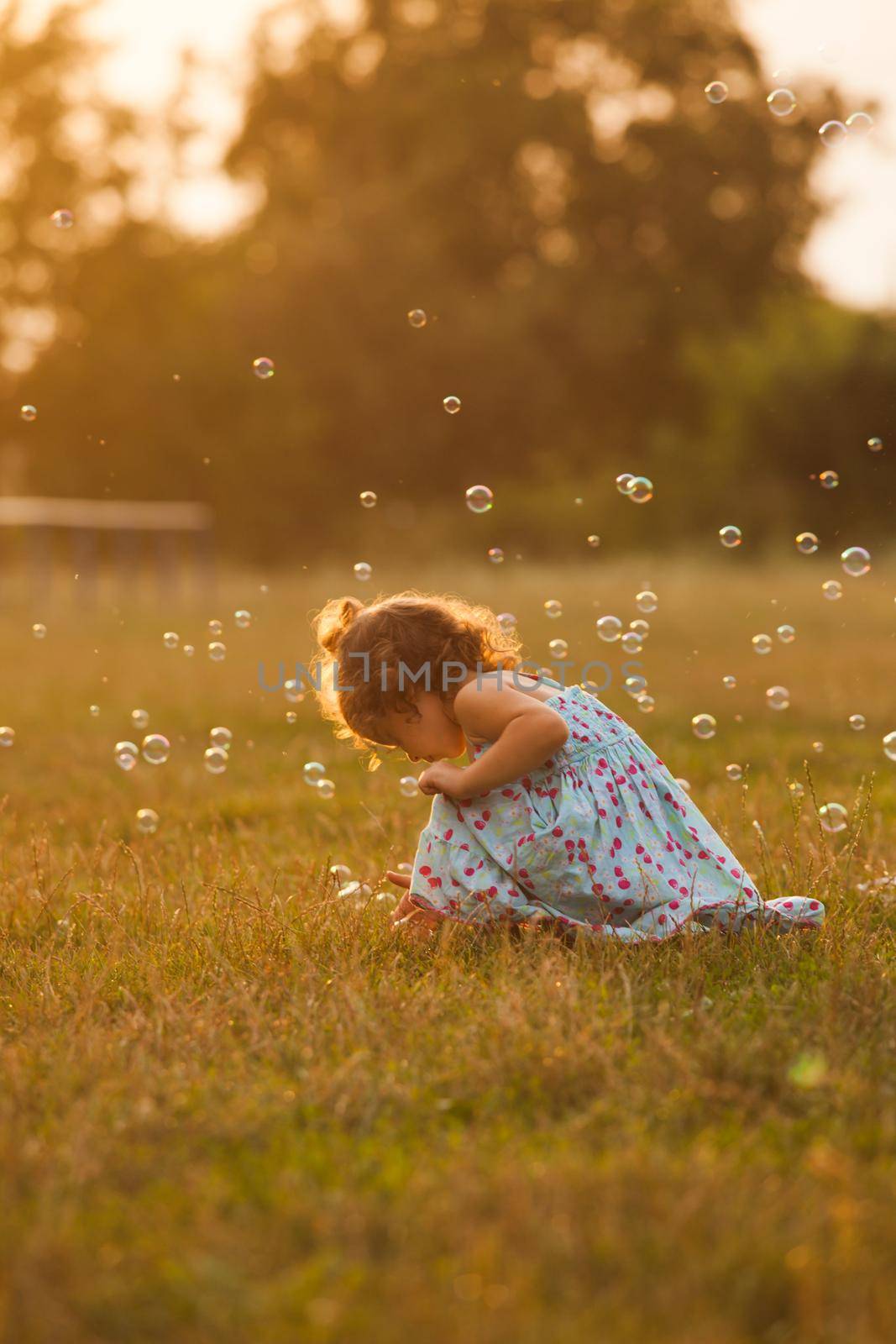 Pretty girl runs for the bubbles in the park on the sunset