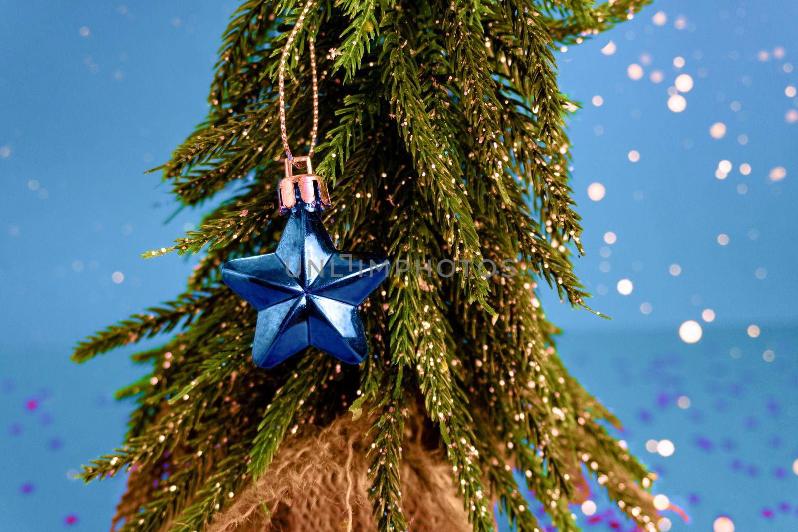 Closeup of blue fragile christmas star toy on a green tree on blue bokeh background. New year and christmas concept.