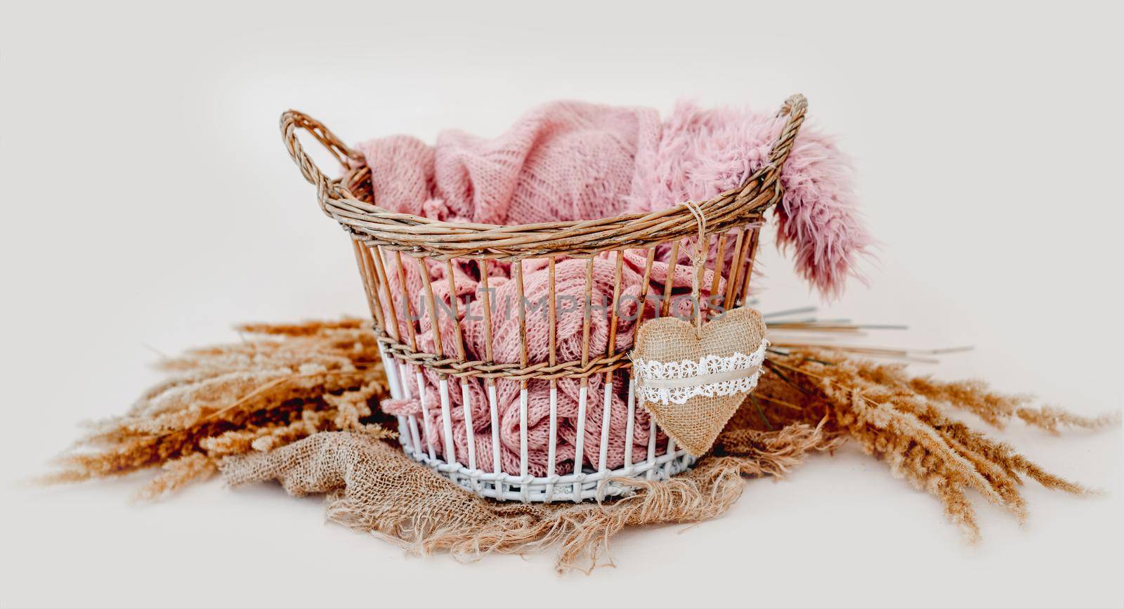 Tiny basket decor for newborn studio photoshoot filled with knitted blanket and toy heart closeup. Infant baby handmade furniture
