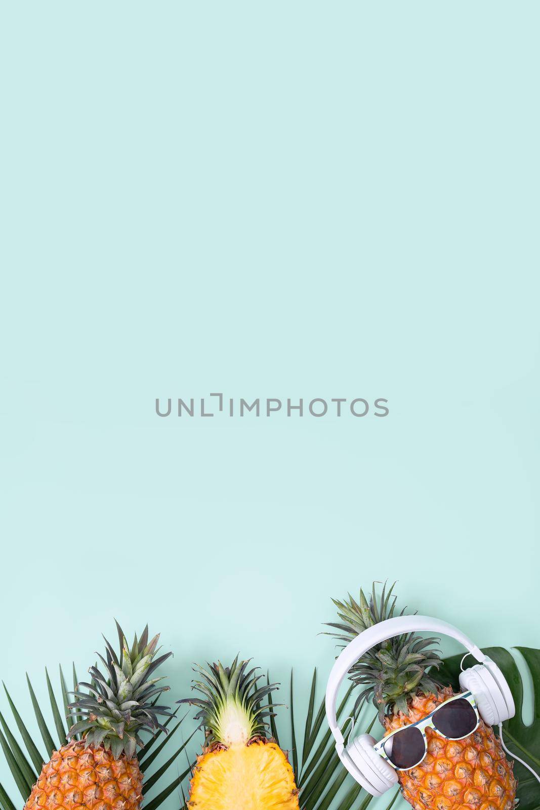 Funny pineapple wearing white headphone, concept of listening music, isolated on colored background with tropical palm leaves, top view, flat lay design. by ROMIXIMAGE