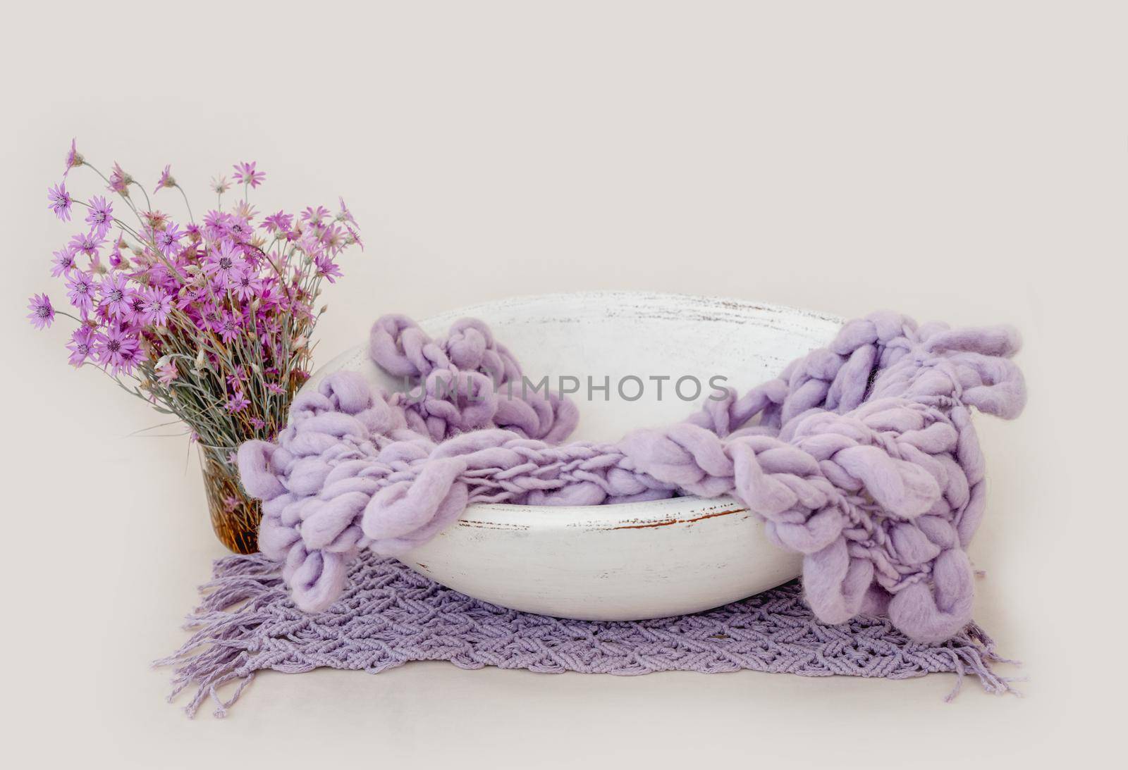 Wooden basin decor for newborn studio photoshoot filled with knitted blanket closeup. Infant baby photo furniture and flower bouquet