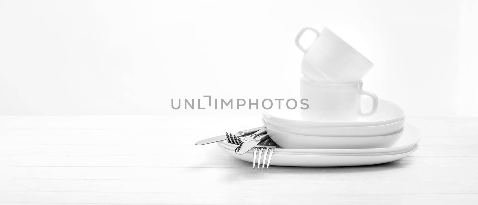 Empty white plates, cups and silver cutlery on light white background. Close-up