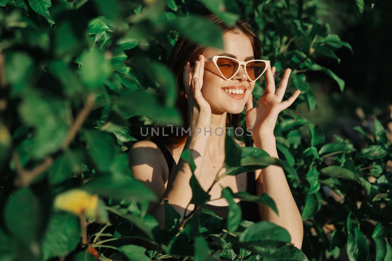 smiling woman wearing sunglasses green leaves nature fashion. High quality photo