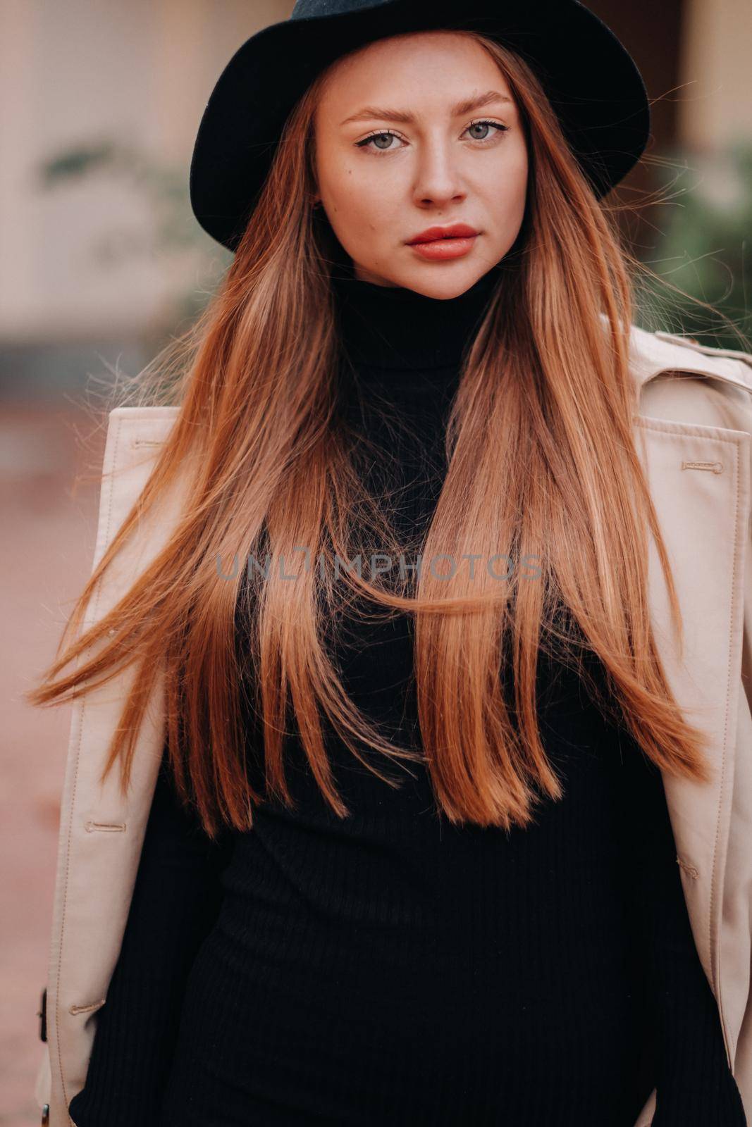 Stylish young woman in a beige coat in a black hat on a city street. Women's street fashion. Autumn clothing.Urban style.