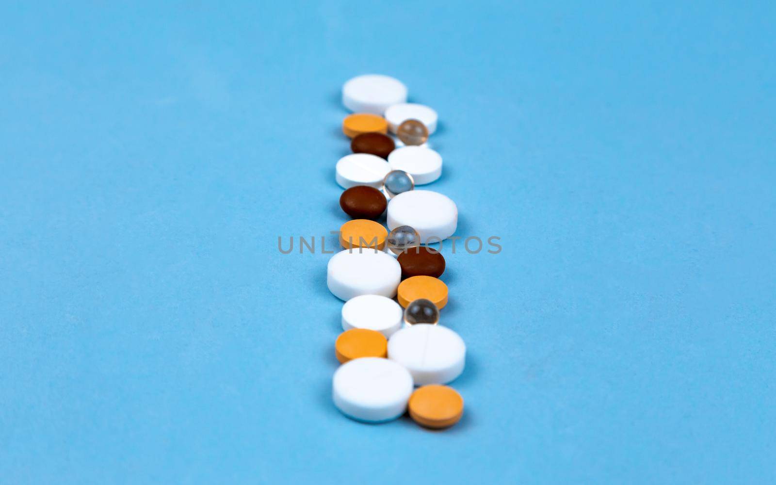 Multi-colored pills and capsules are laid out on a blue background in a row with copy space for text.