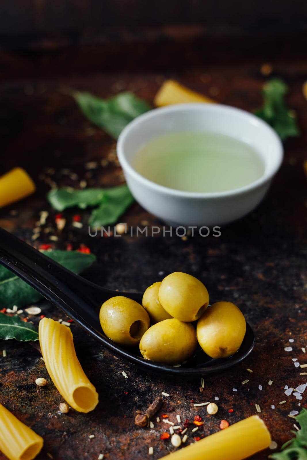 Olives in black spoon surrounded by other ingredients.