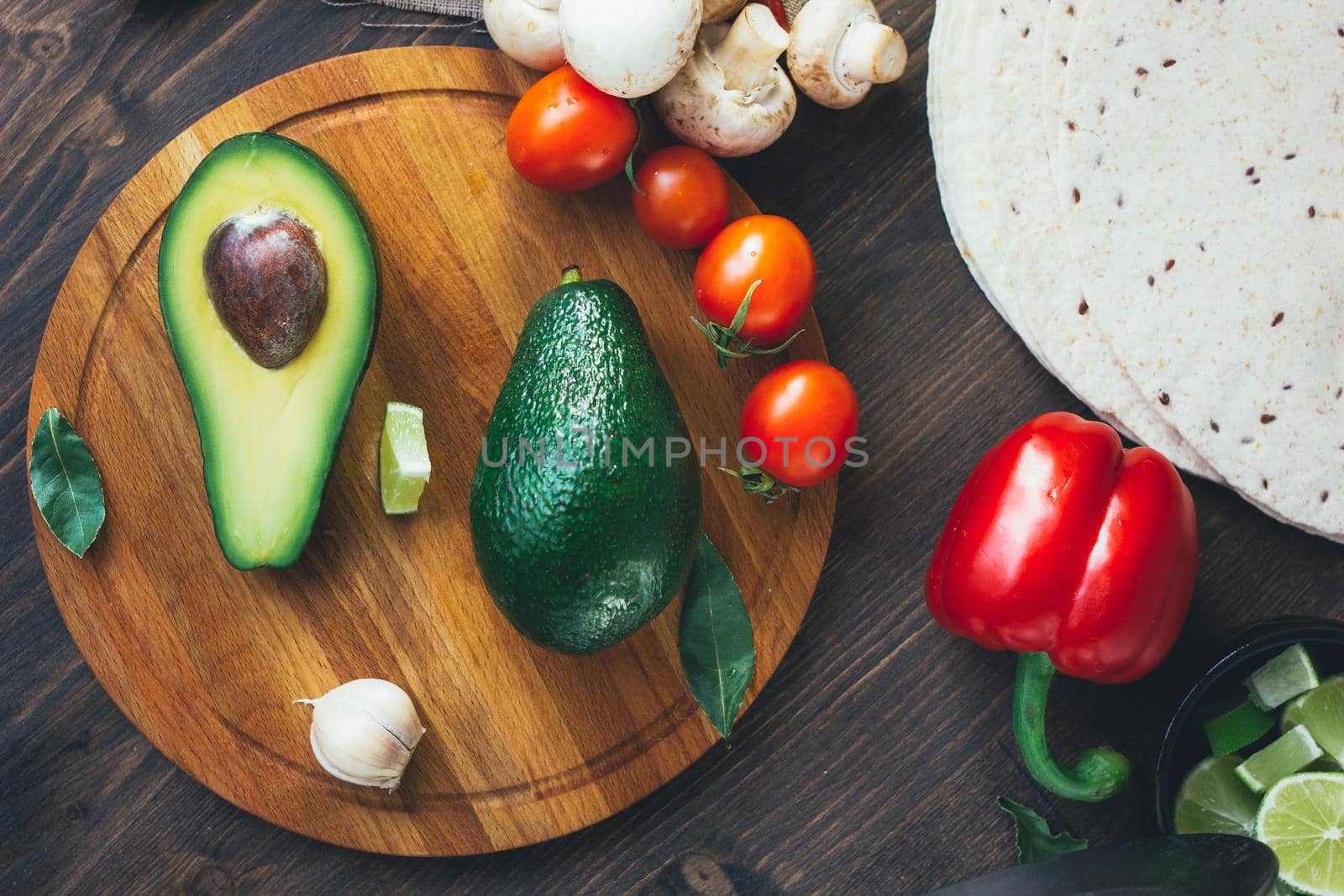 Top view of avocado standing on wooden board surrounded by vegetables