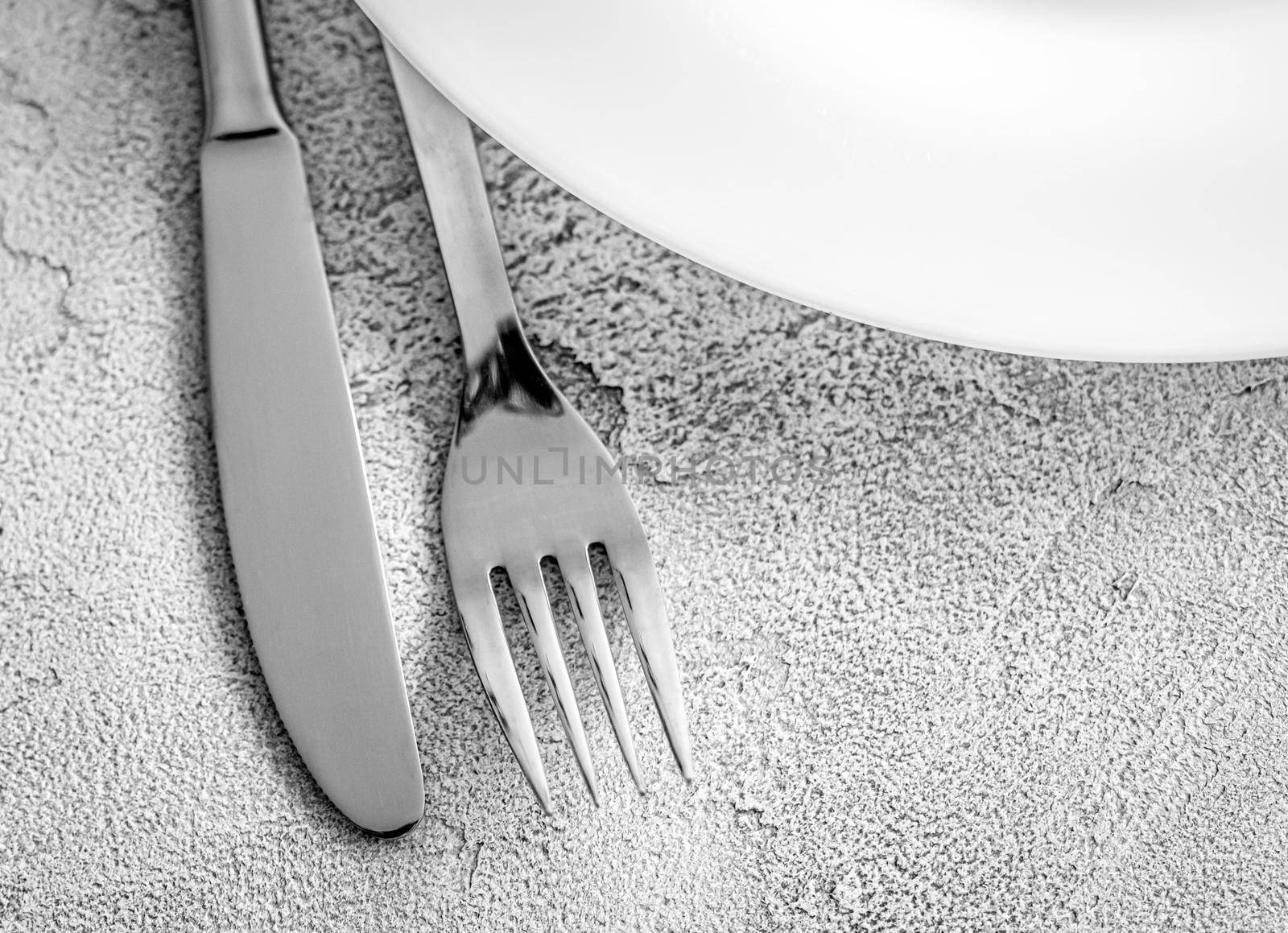 Stainless fork and knife with white plate, top view with copy space