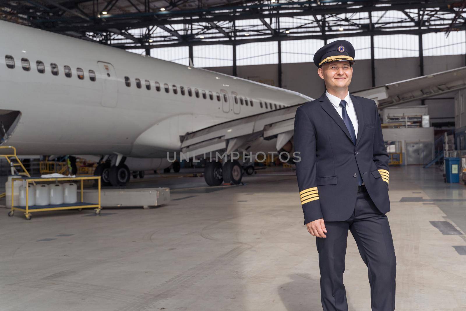 Smiling pilot posing against the backdrop of the aircraft in the hangar by Yaroslav_astakhov