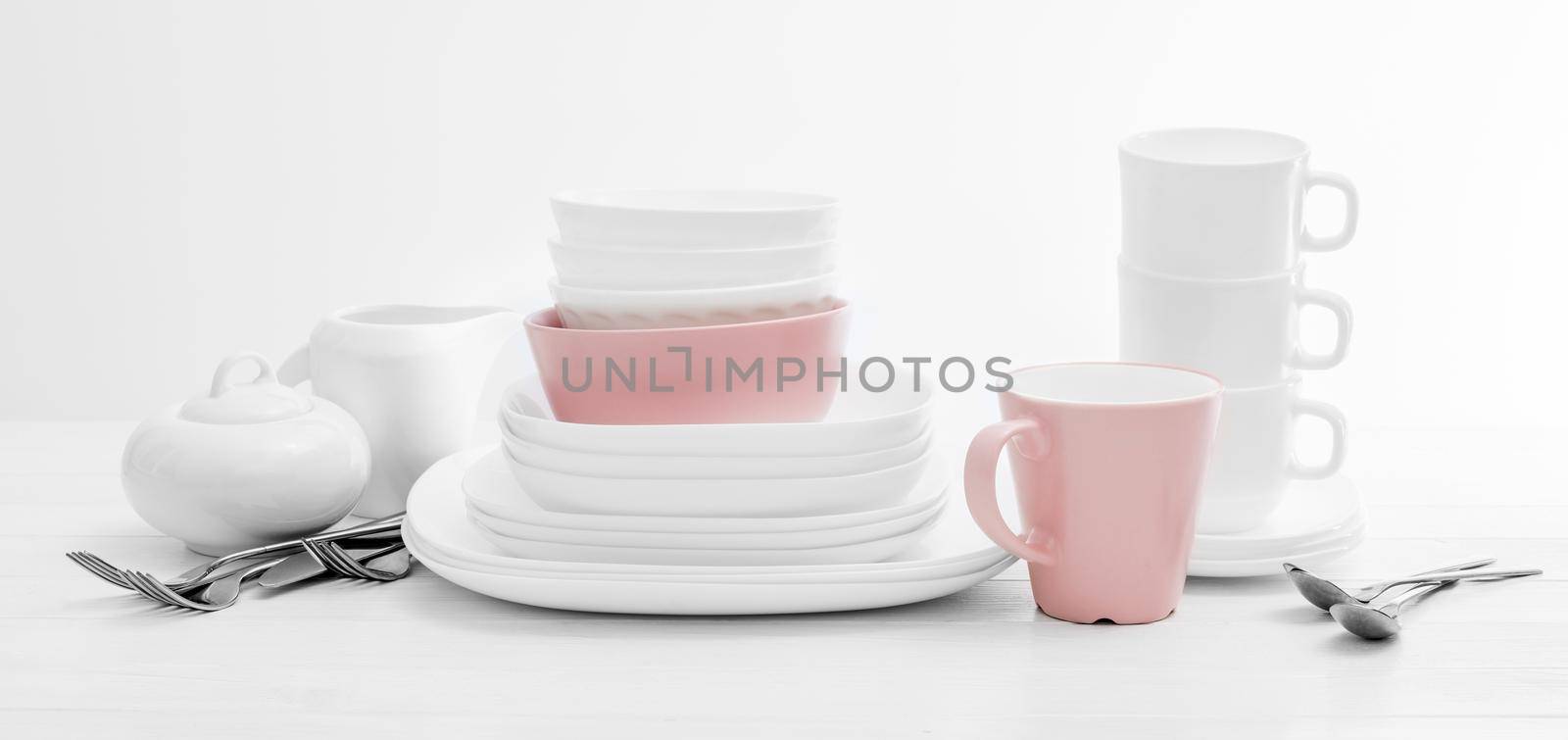 White and pink plates, sugar bowl and mugs on light background. Ceramic tableware.