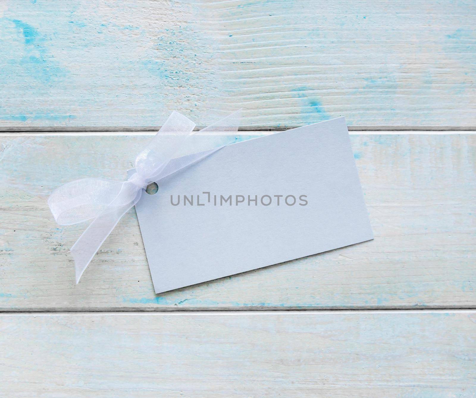 Paper greeting card or label with delicate blue ribbon on painted wooden background. Place for text. Holiday greeting card for Valentine's Day,
