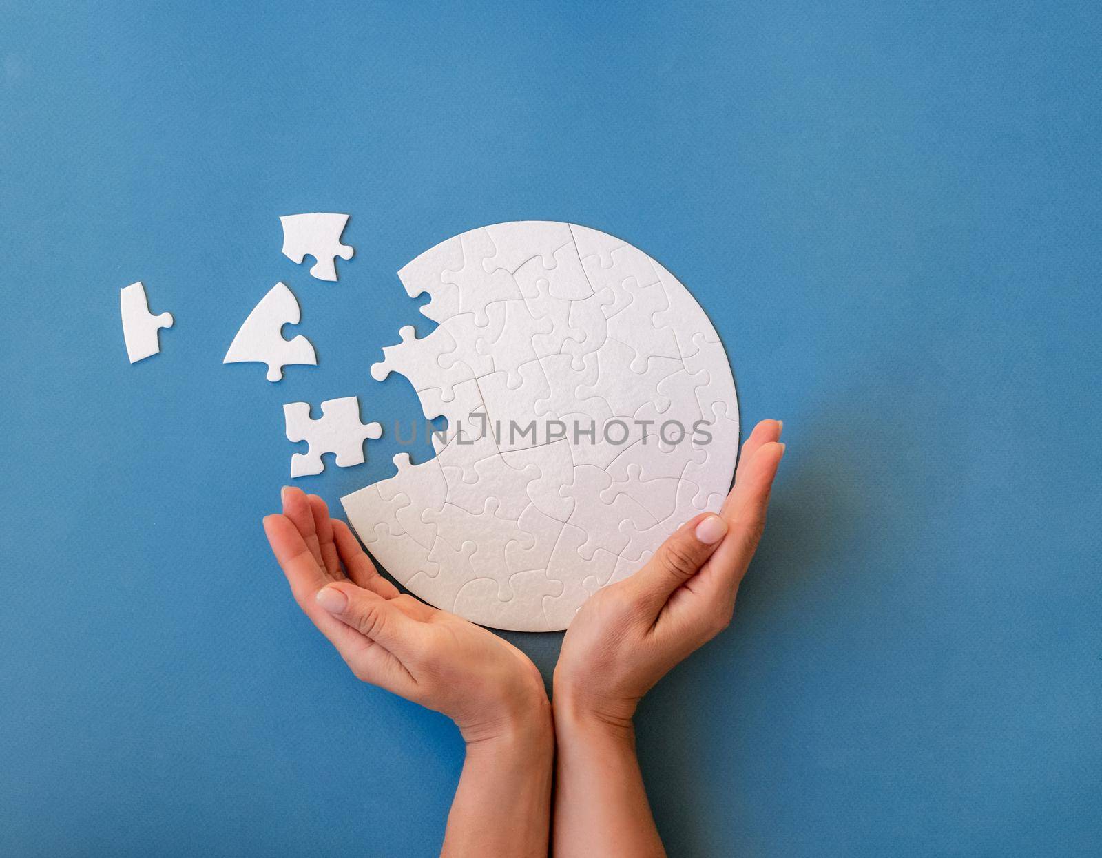Hands holding unfinished jigsaw puzzle in shape on blue background